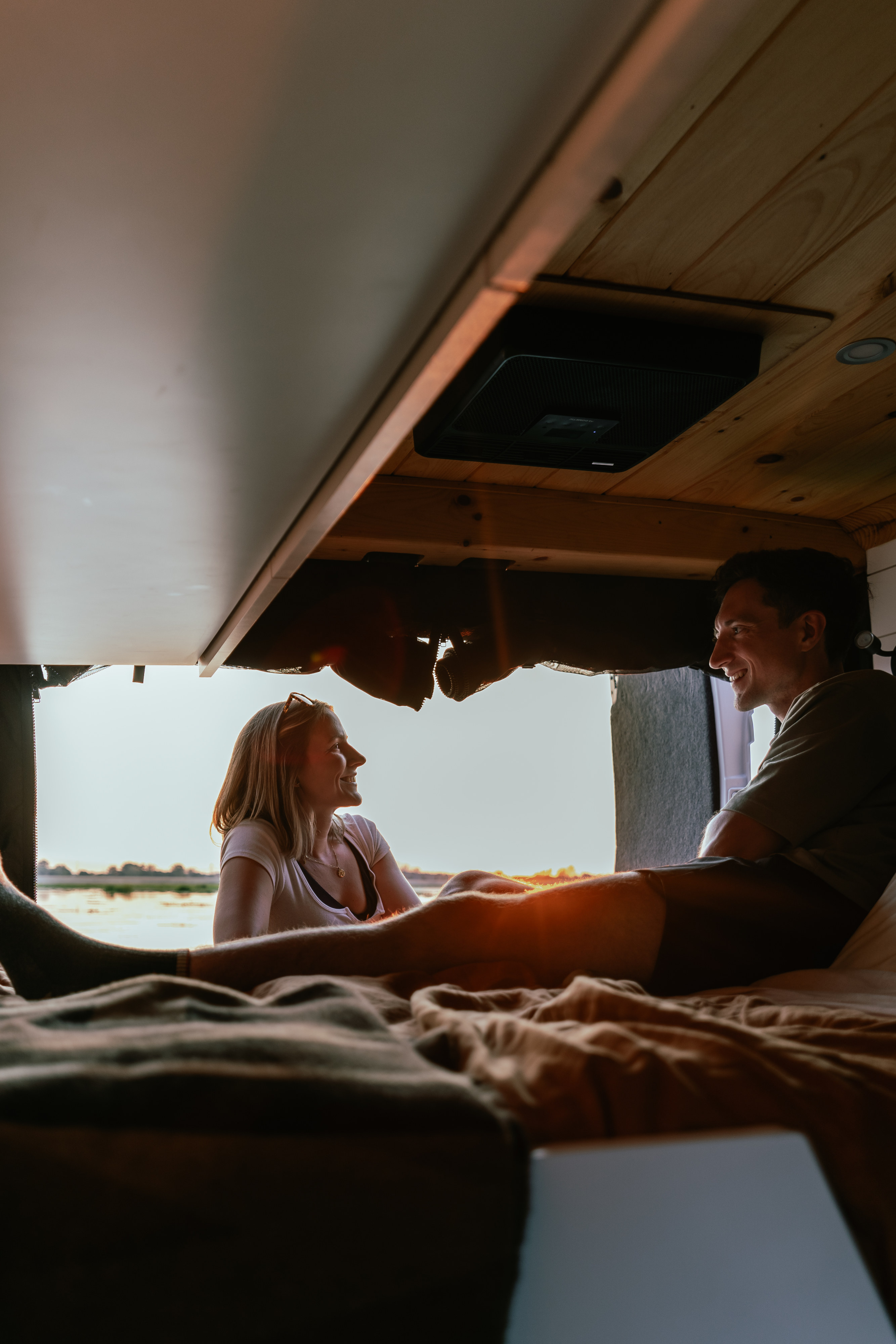 Inside a cozy rv rental, a happy couple relaxes on the bed, enjoying sunset views. Van life travel for two.. Ram Promaster 2022