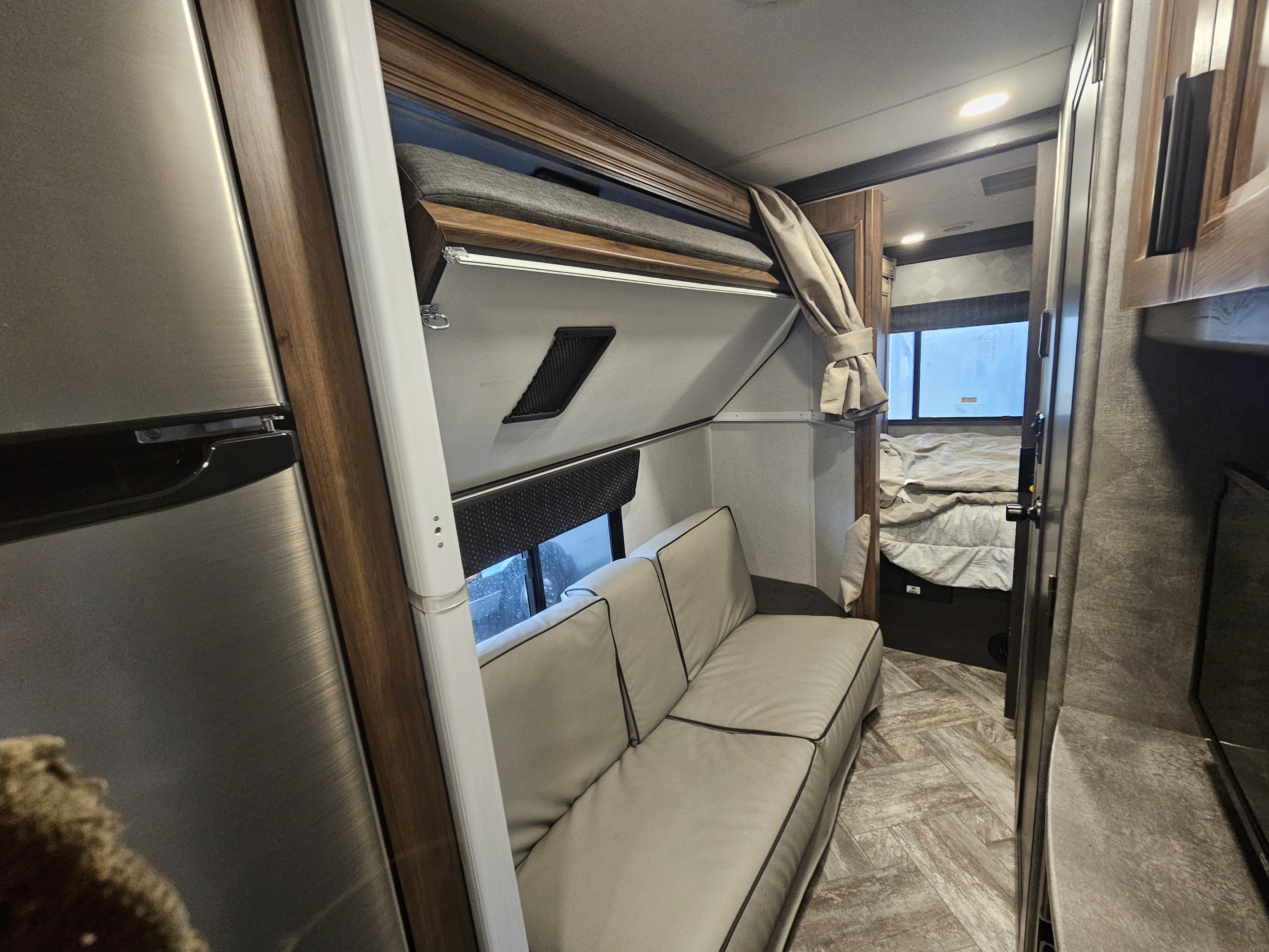 RV rental interior with a living space featuring a sofa, upper bunk bed, and a glimpse into the rear bedroom.. Forester LE 2021