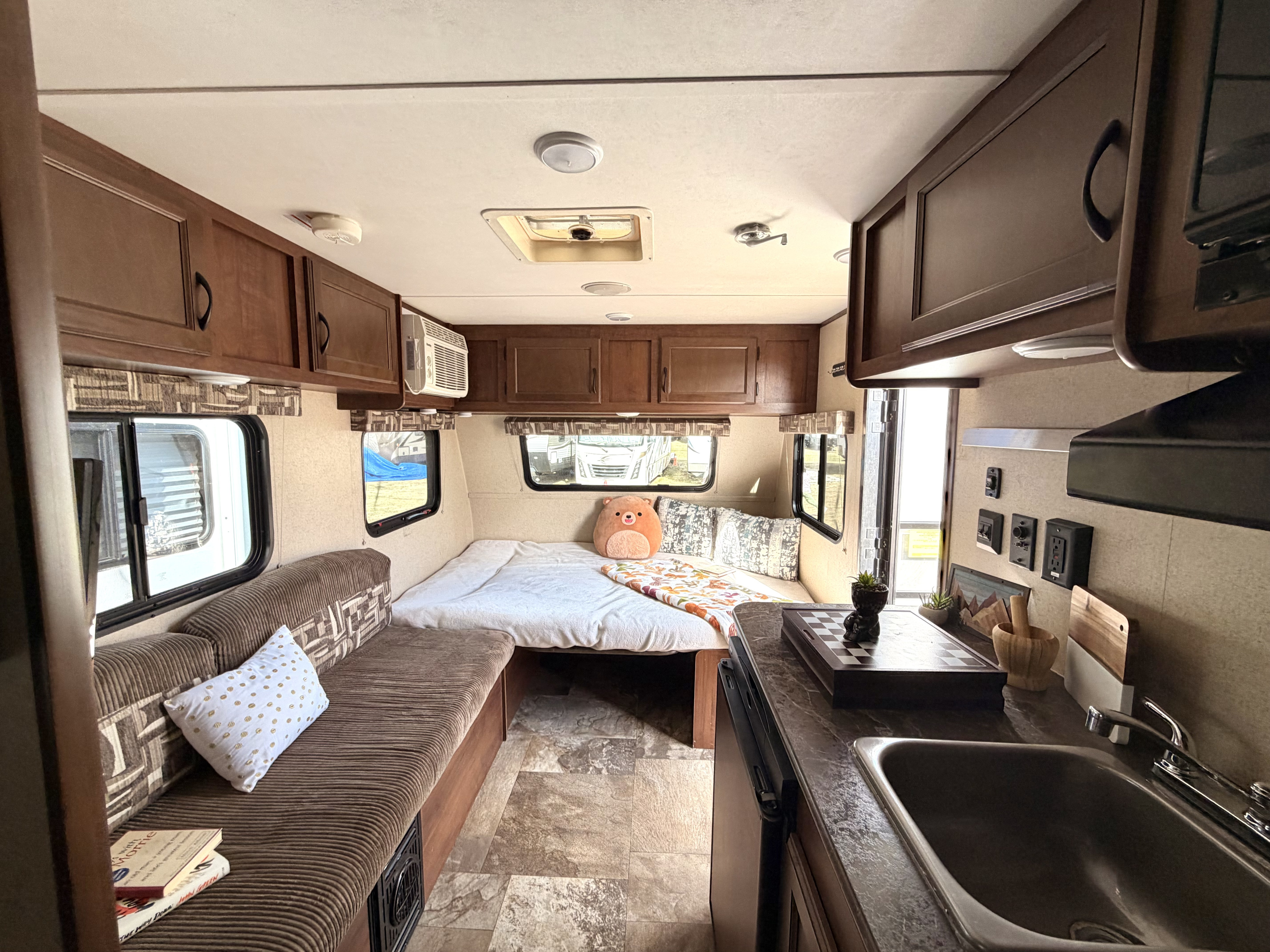 This inviting RV rental interior features a cozy bed, compact kitchen with sink, and a comfy dinette with windows.. Jayco Jay Flight SLX 2015