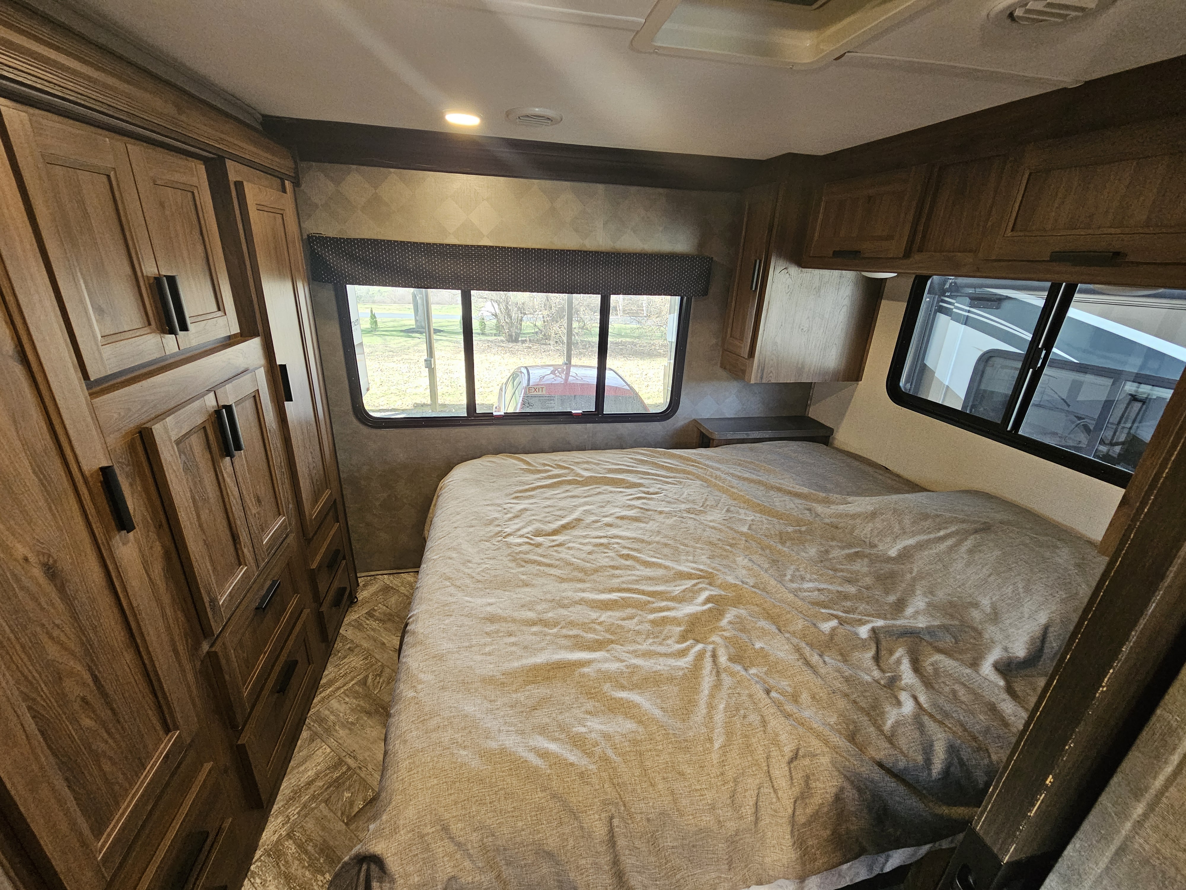 Inside an RV rental bedroom, showcasing a comfortable bed, wood storage, and bright windows looking outside.. Forester LE 2021