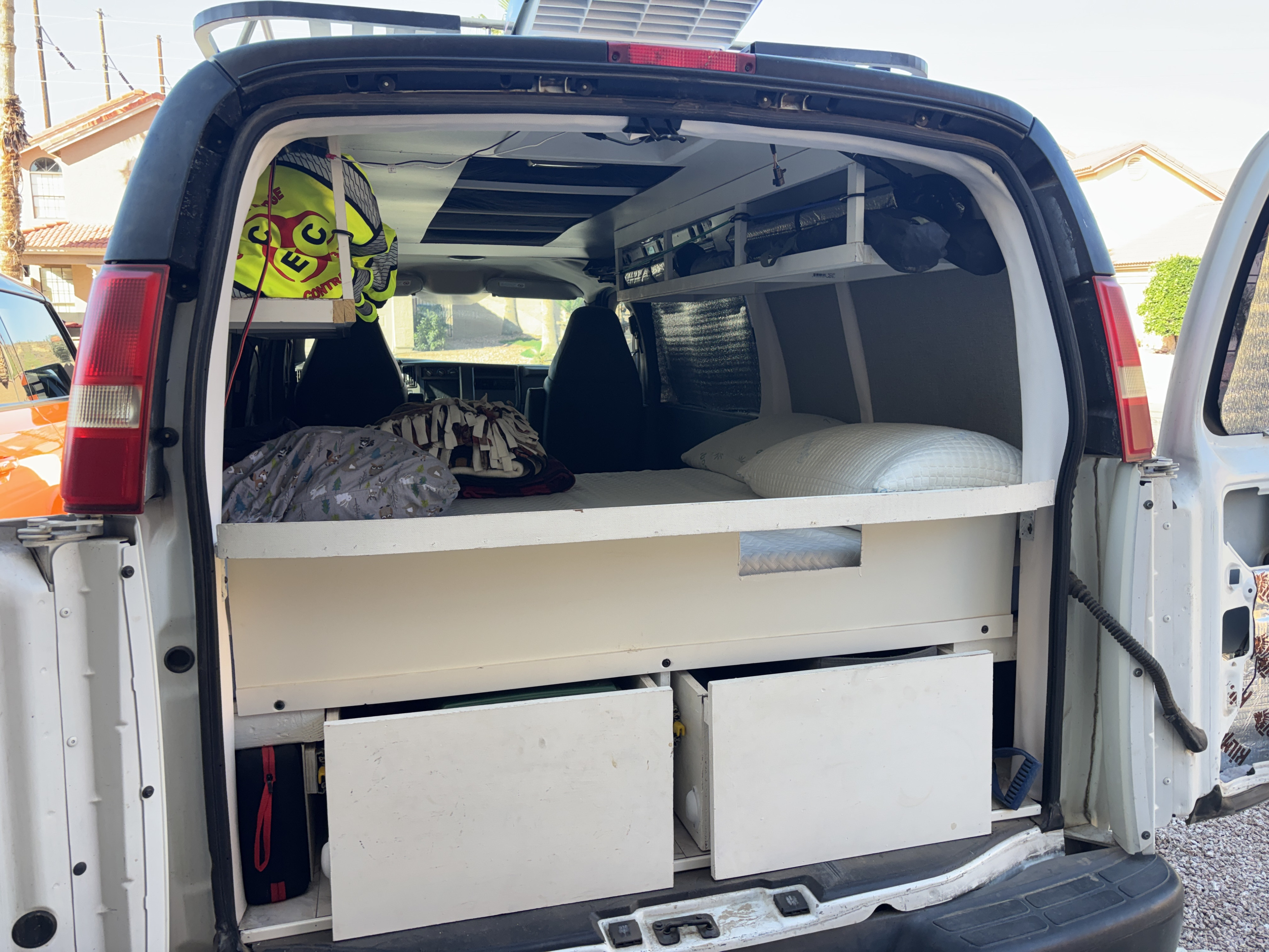 This RV rental showcases a DIY camper van conversion with a bed, pillows, and integrated storage, seen from the rear.. Chevrolet Express 1500 AWD 2007