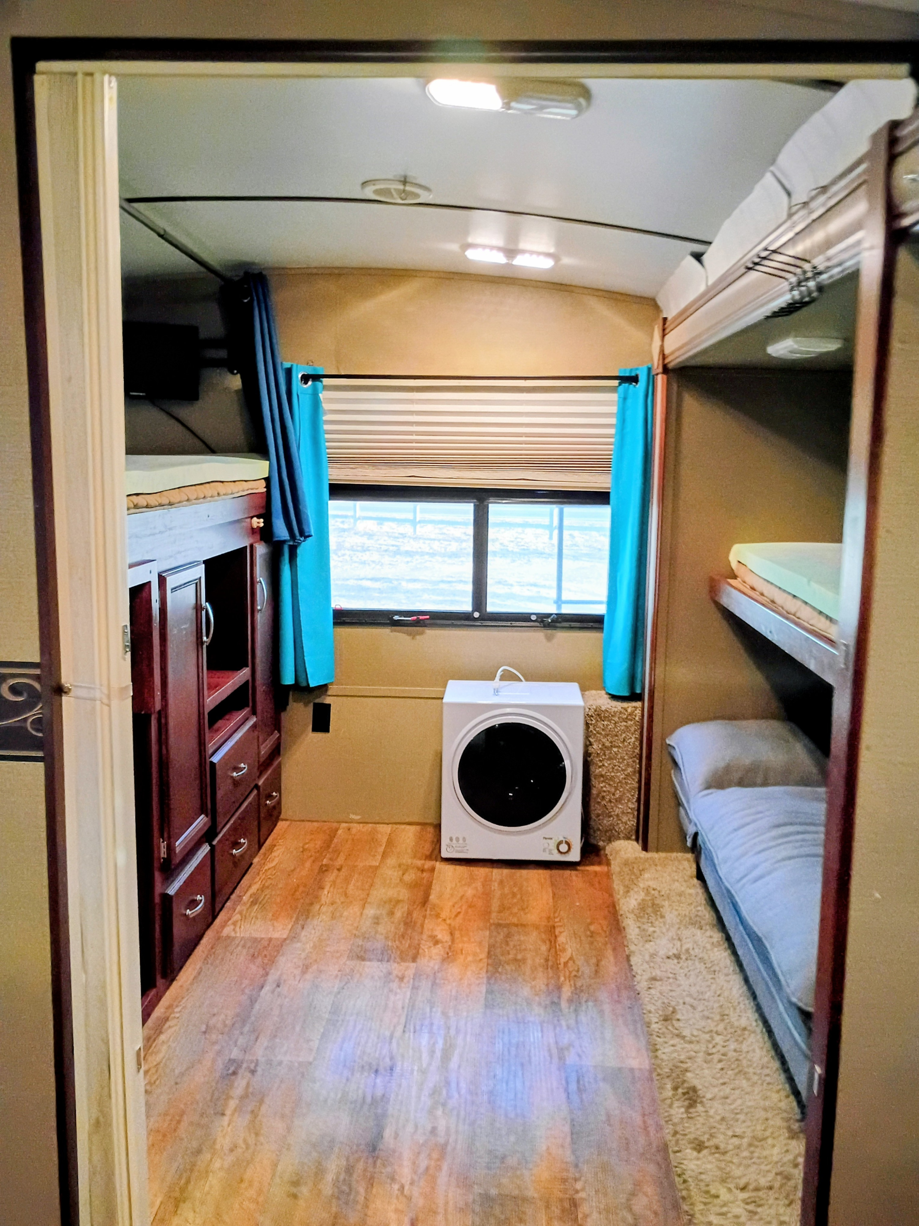 RV rental bunk room with bunk beds, wooden cabinetry, window, and a portable dryer on a wood-look floor.. Keystone RV Outback Super-Lite 2015