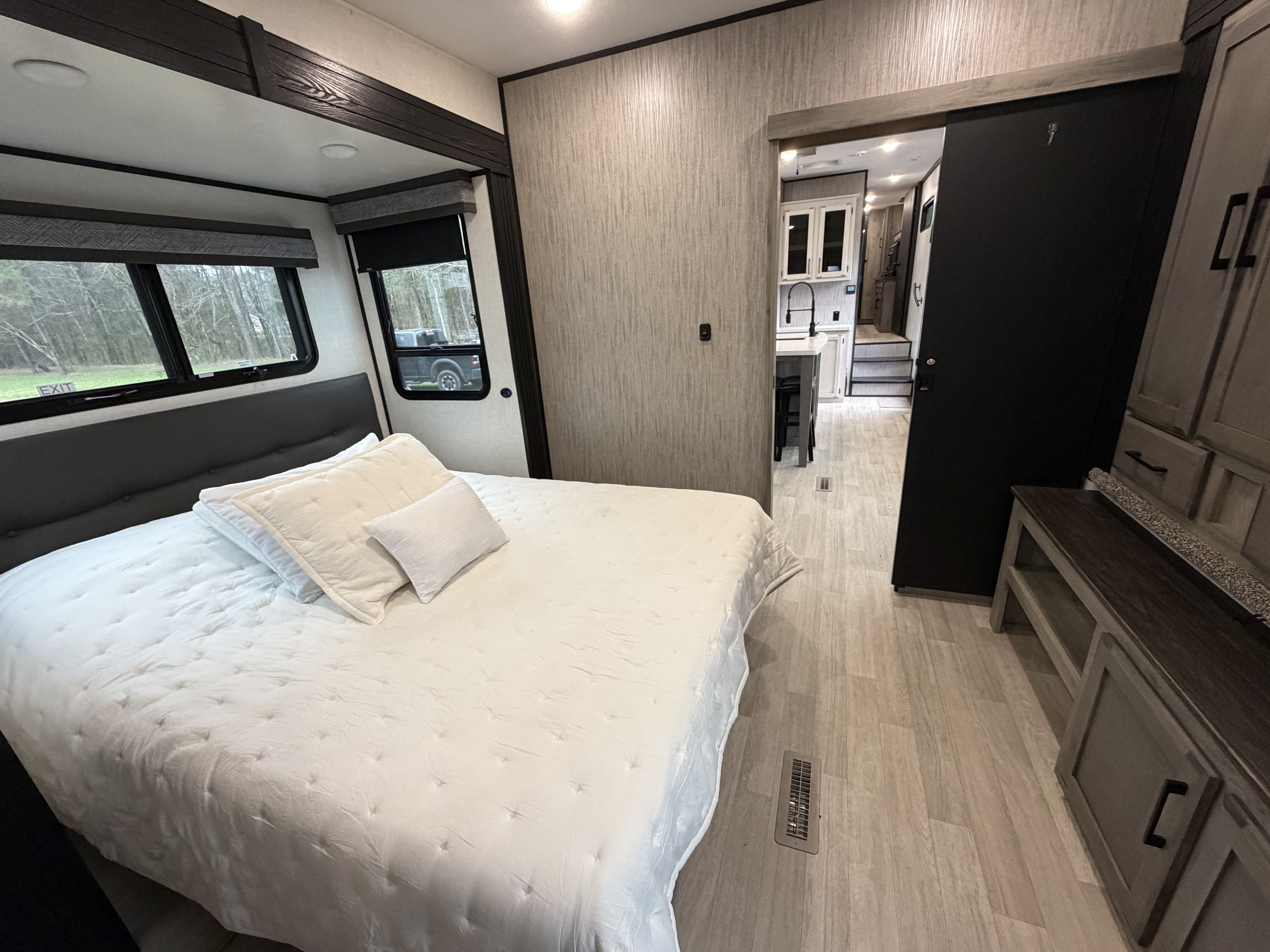 Cozy rv rental bedroom with white bedding, a modern headboard, and a view into the spacious kitchen area. Perfect for travel.. Durango Durango Fifth Wheel 2023