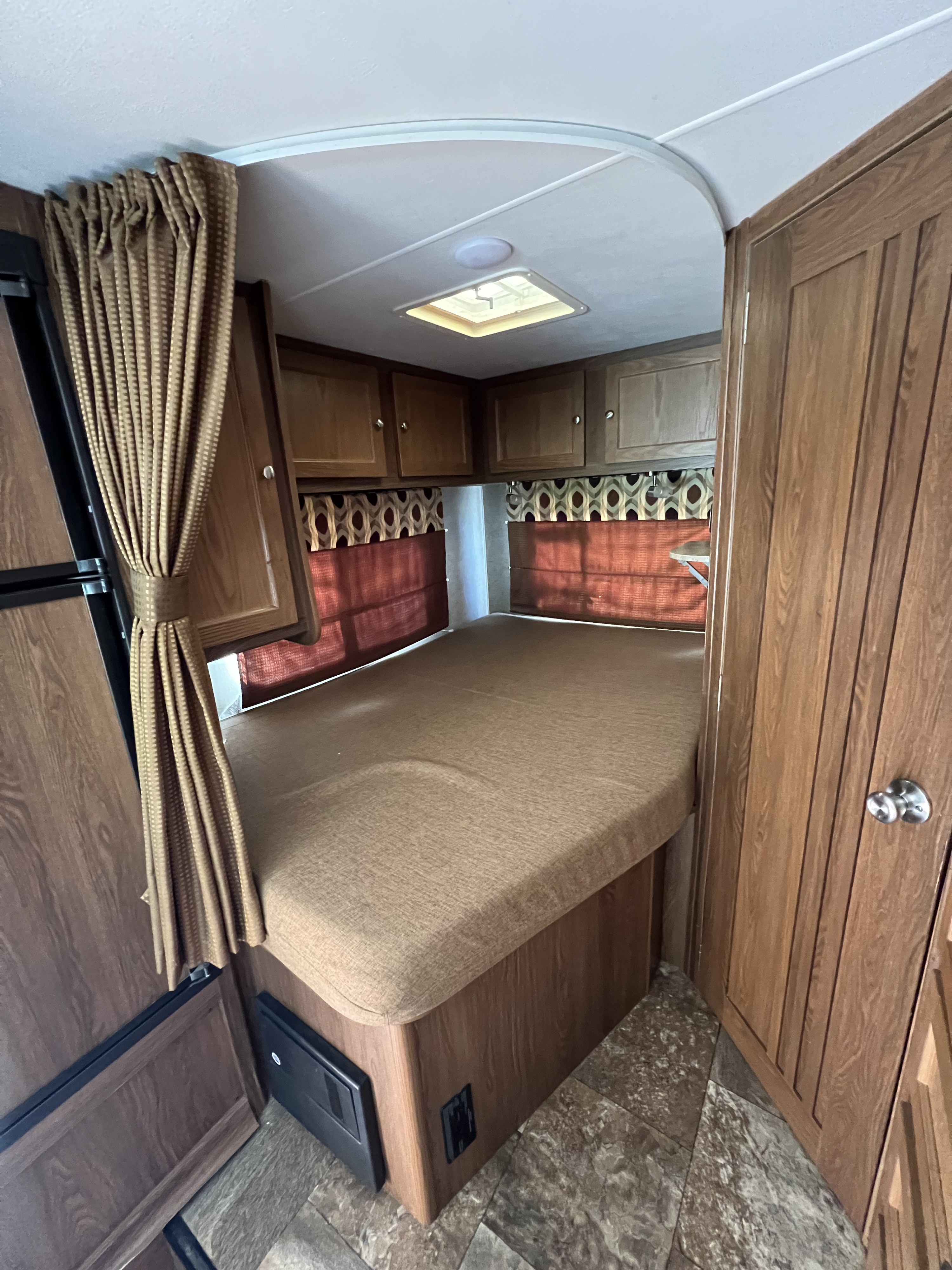 Cozy RV rental bedroom featuring a comfortable bed, wooden overhead cabinets, and patterned window treatments for a pleasant travel experience.. Forest River Coachmen Leprechaun 2017