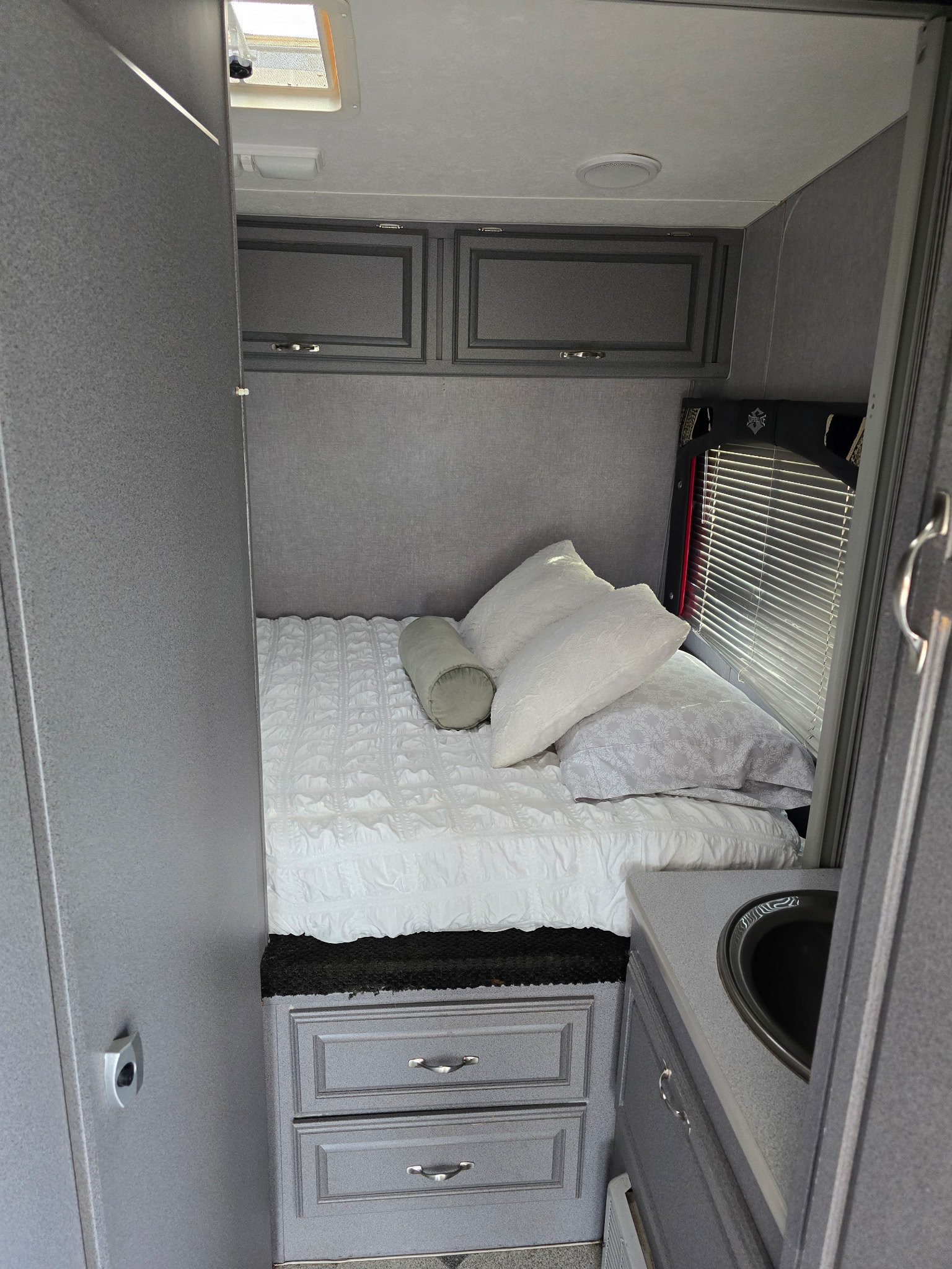 This RV rental bedroom offers a comfortable bed, overhead cabinets, window with blinds, and a built-in sink in muted gray tones.. Weekend Warrior Fs2300superlite 2007
