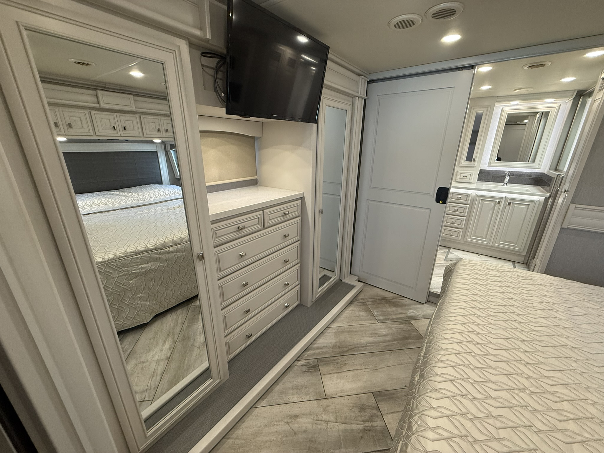 Spacious RV rental interior: a modern bedroom with mirrored closet, dresser, TV, and access to a stylish en-suite bathroom.. Fleetwood Discovery LXE 2021