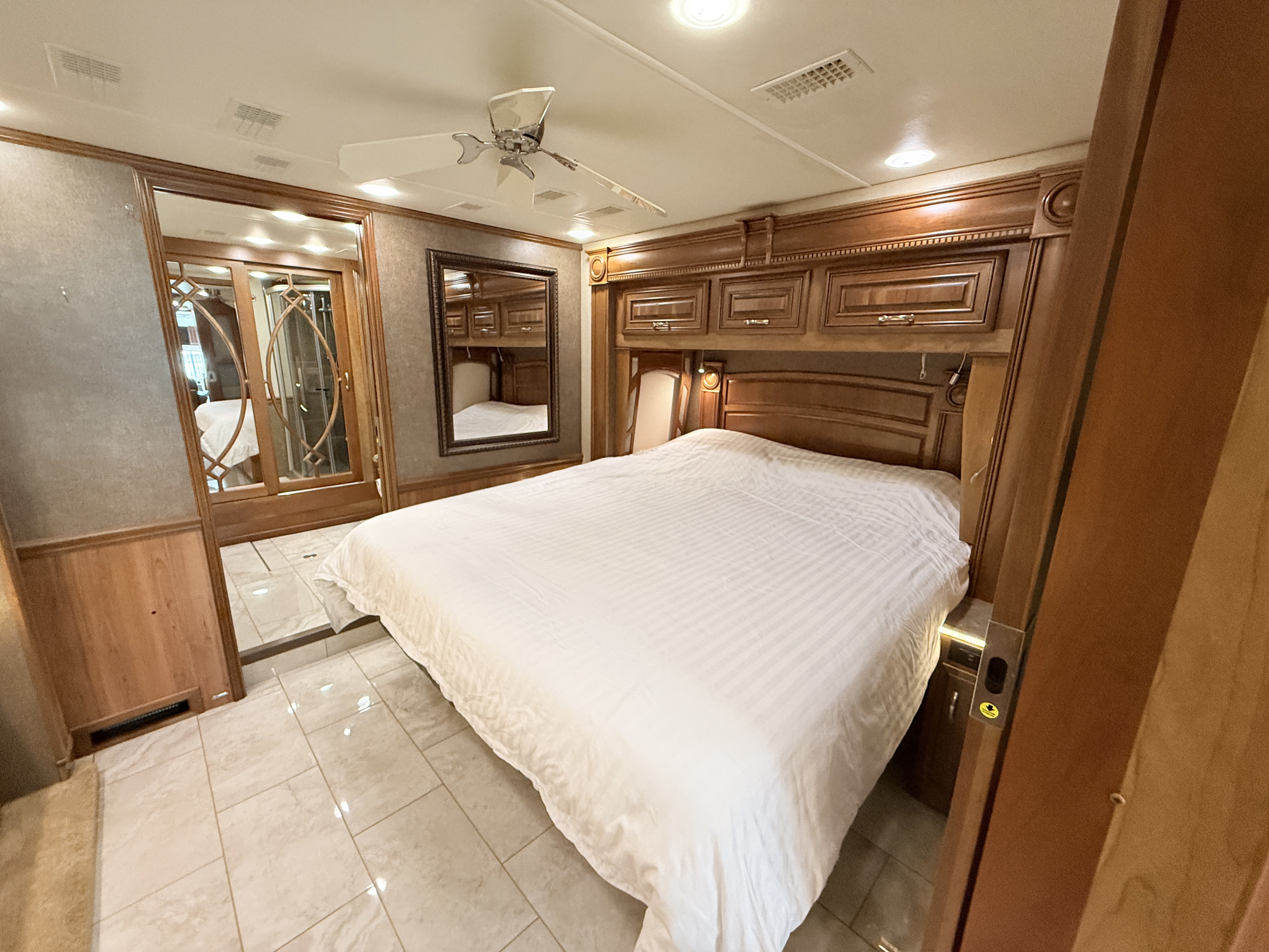 Spacious RV rental bedroom featuring a large bed, elegant wooden cabinetry, ceiling fan, and mirrored closet doors.. Entegra Coach Anthem 2019