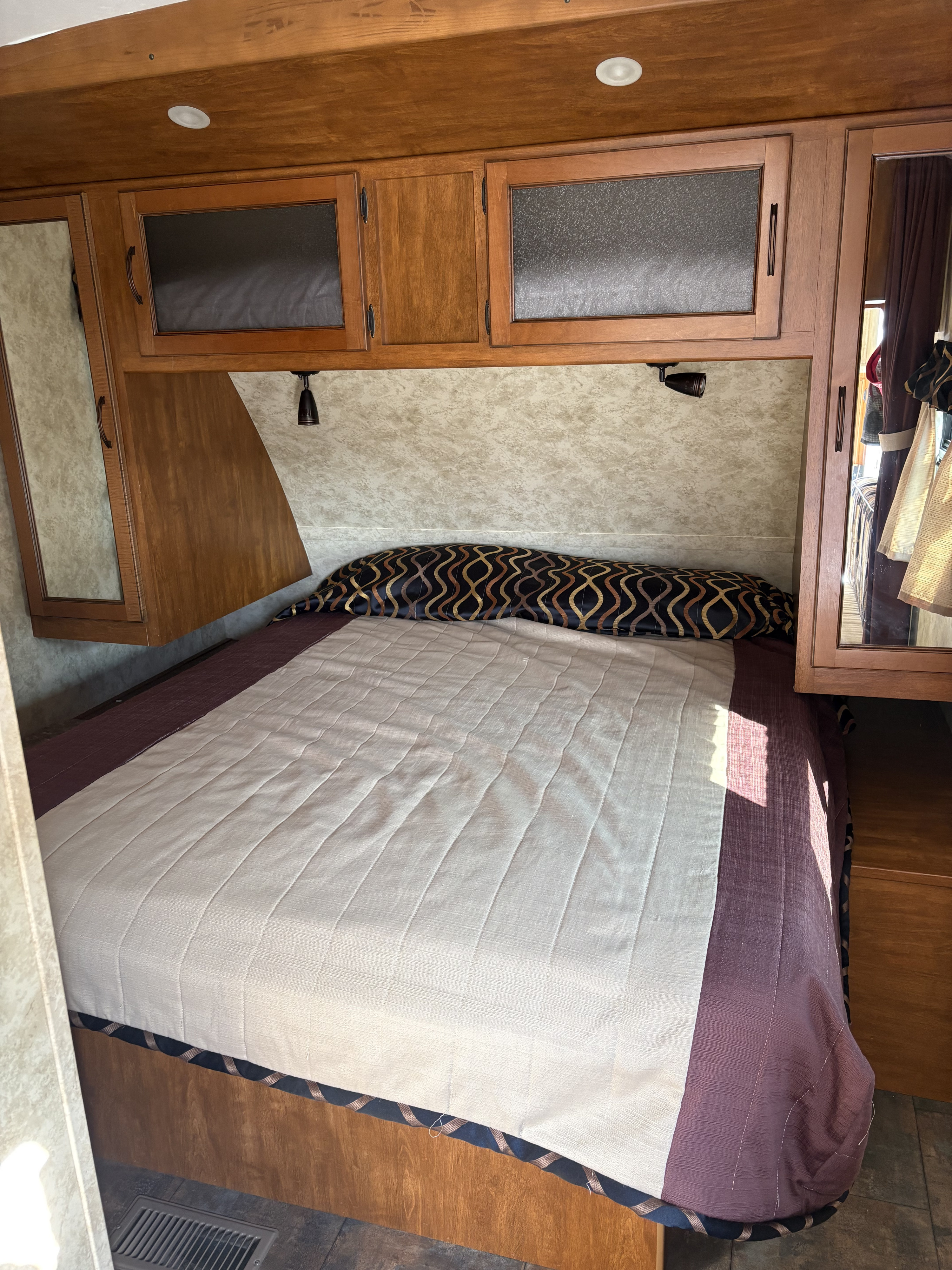 Cozy RV rental bedroom featuring a full bed, overhead cabinets, and reading lamps for your next adventure.. Keystone RV Bullet Ultra Lite 2011