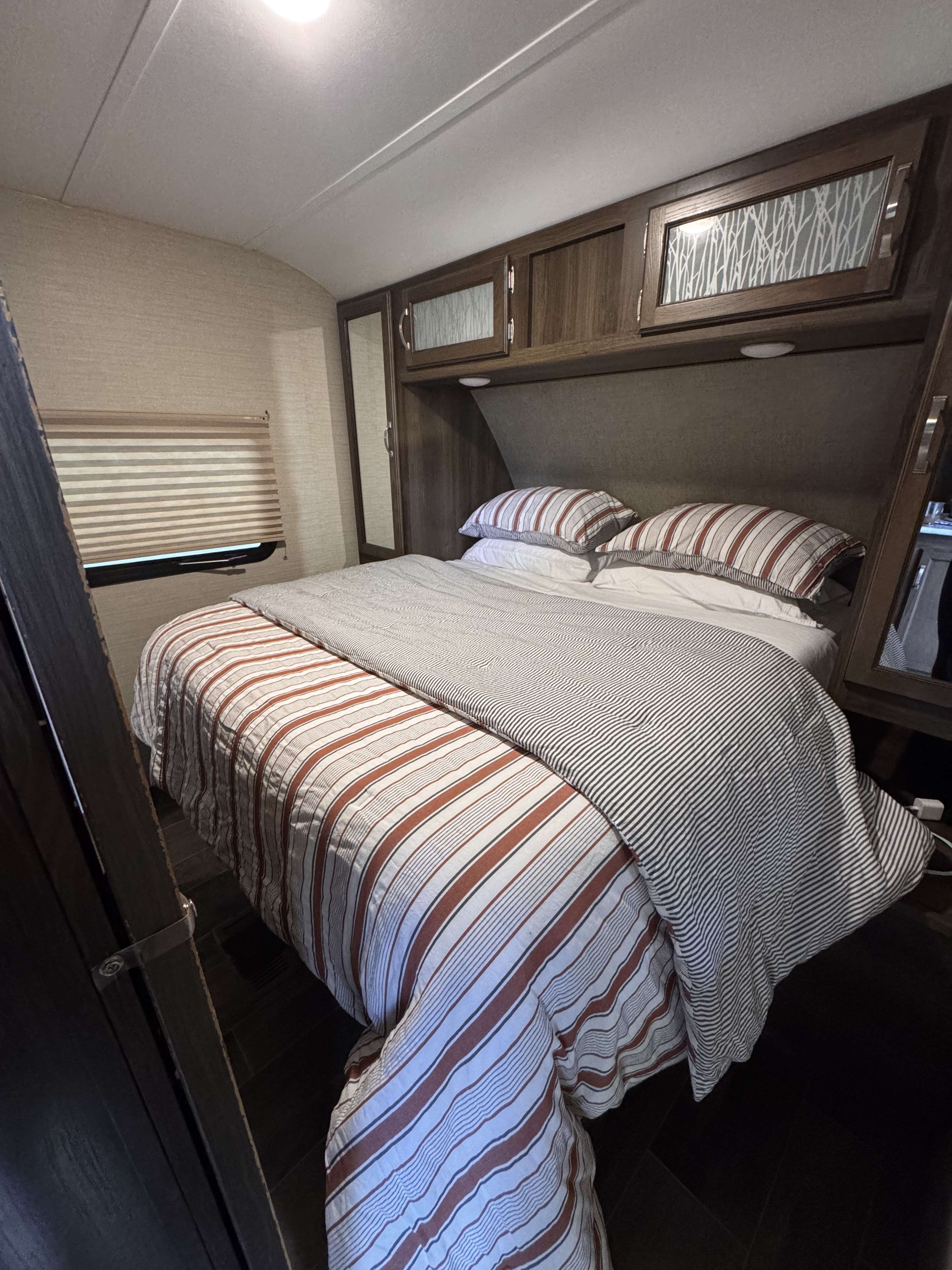 Cozy rv rental bedroom features striped bedding, overhead cabinets, and a window shade, ready for adventure.. Keystone RV Bullet Ultra Lite 2019