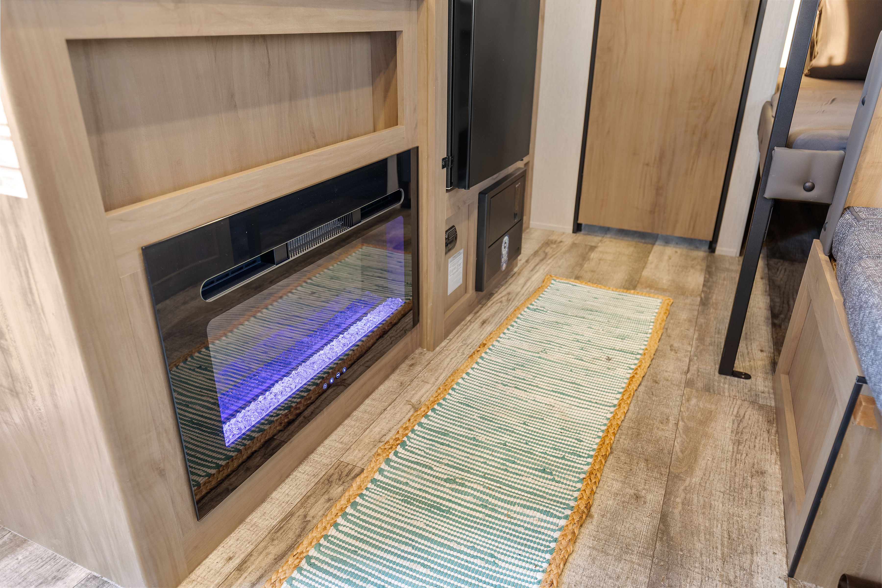 RV rental living space featuring a glowing electric fireplace, light wood cabinetry, a colorful floor runner, and practical flooring.. Forest River Wolf Den 16EV 2025