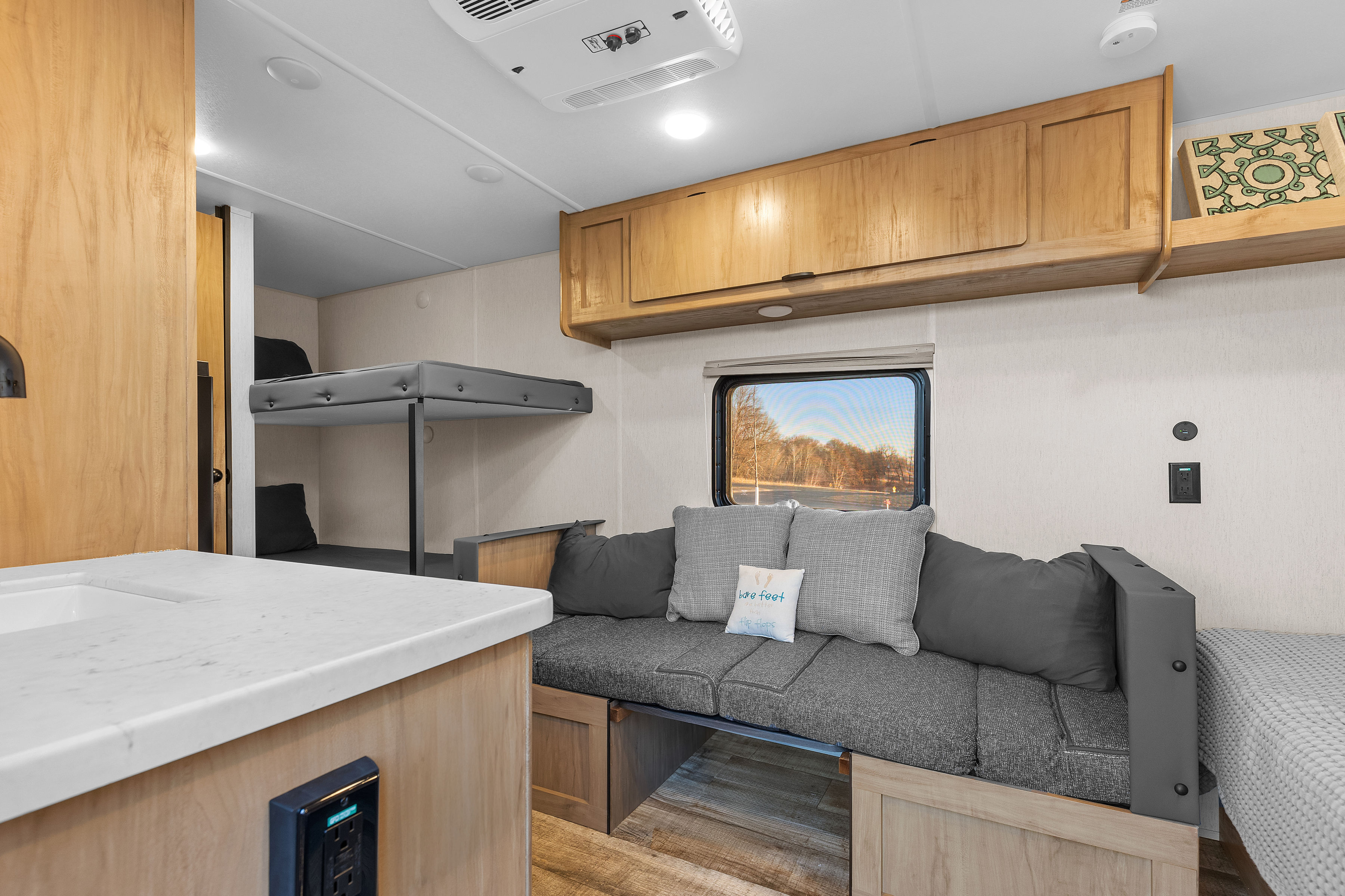 Spacious RV rental interior with light wood cabinetry, bunk beds, and a comfy dinette with cushions. Sink and window also visible.. Forest River Wolf Den 16EV 2025
