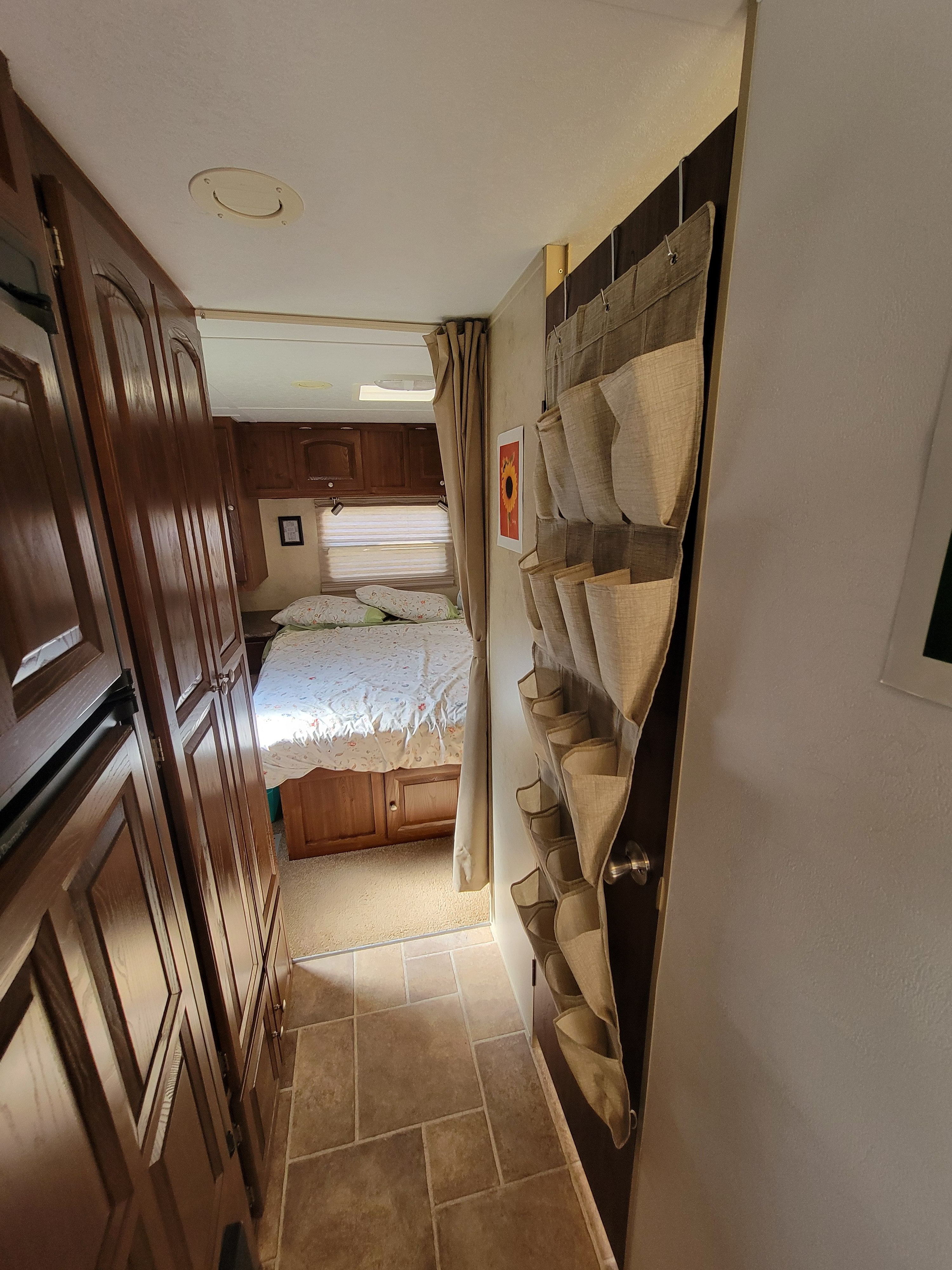 RV rental interior view: a narrow hallway with wood cabinets and a hanging organizer leads to a cozy bedroom.. Forest River Flagstaff V-Lite 2010