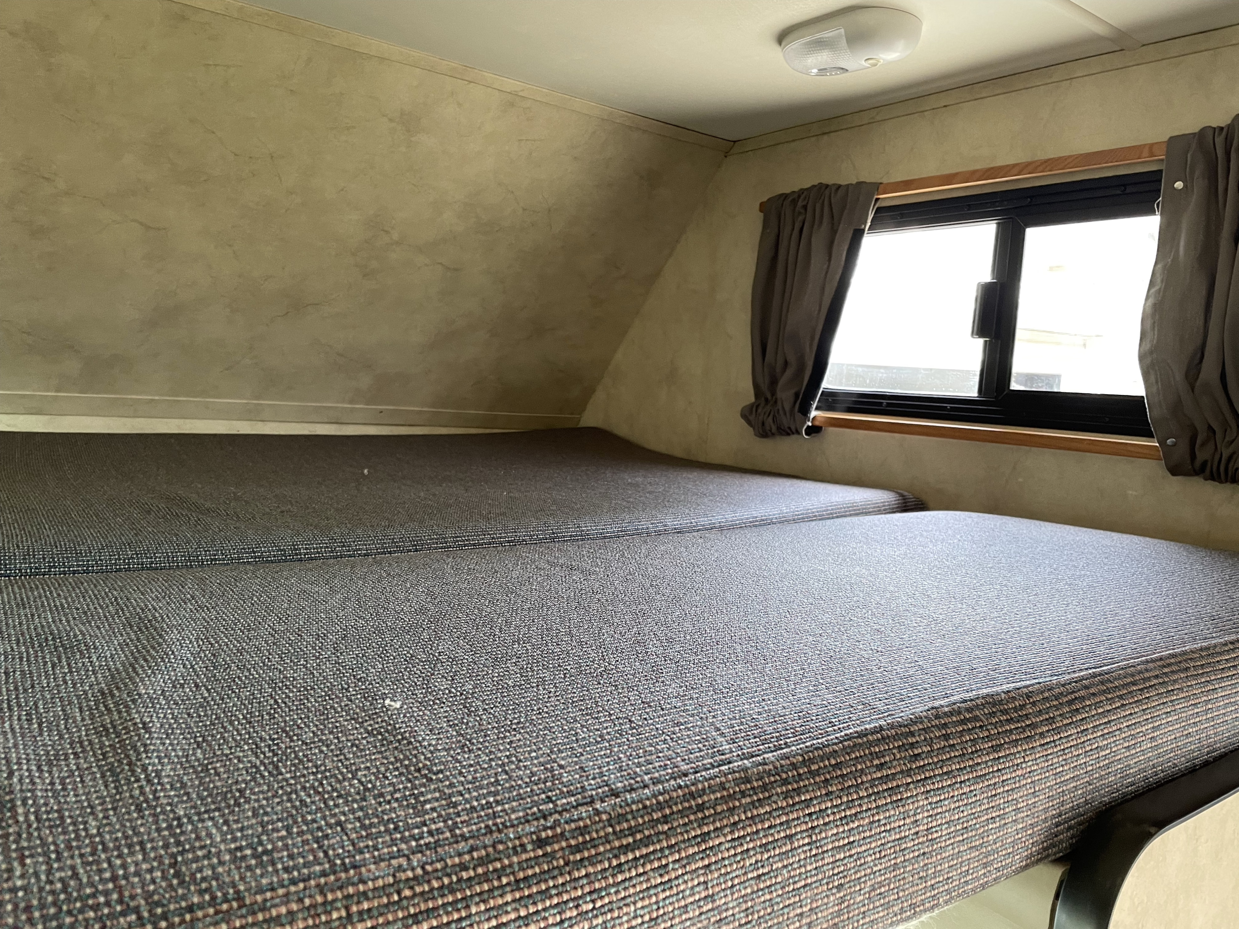 RV rental interior showing a bunk bed area with two mattresses, a side window with curtains, and an overhead light.. Majestic Leisure Craft Cutaway 2012