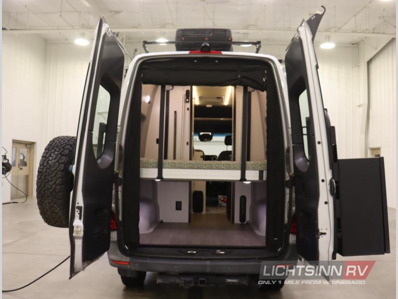 RV rental: Rear view of white camper van with open doors, revealing interior bed, storage, and spare tire.. Winnebago Revel 2020