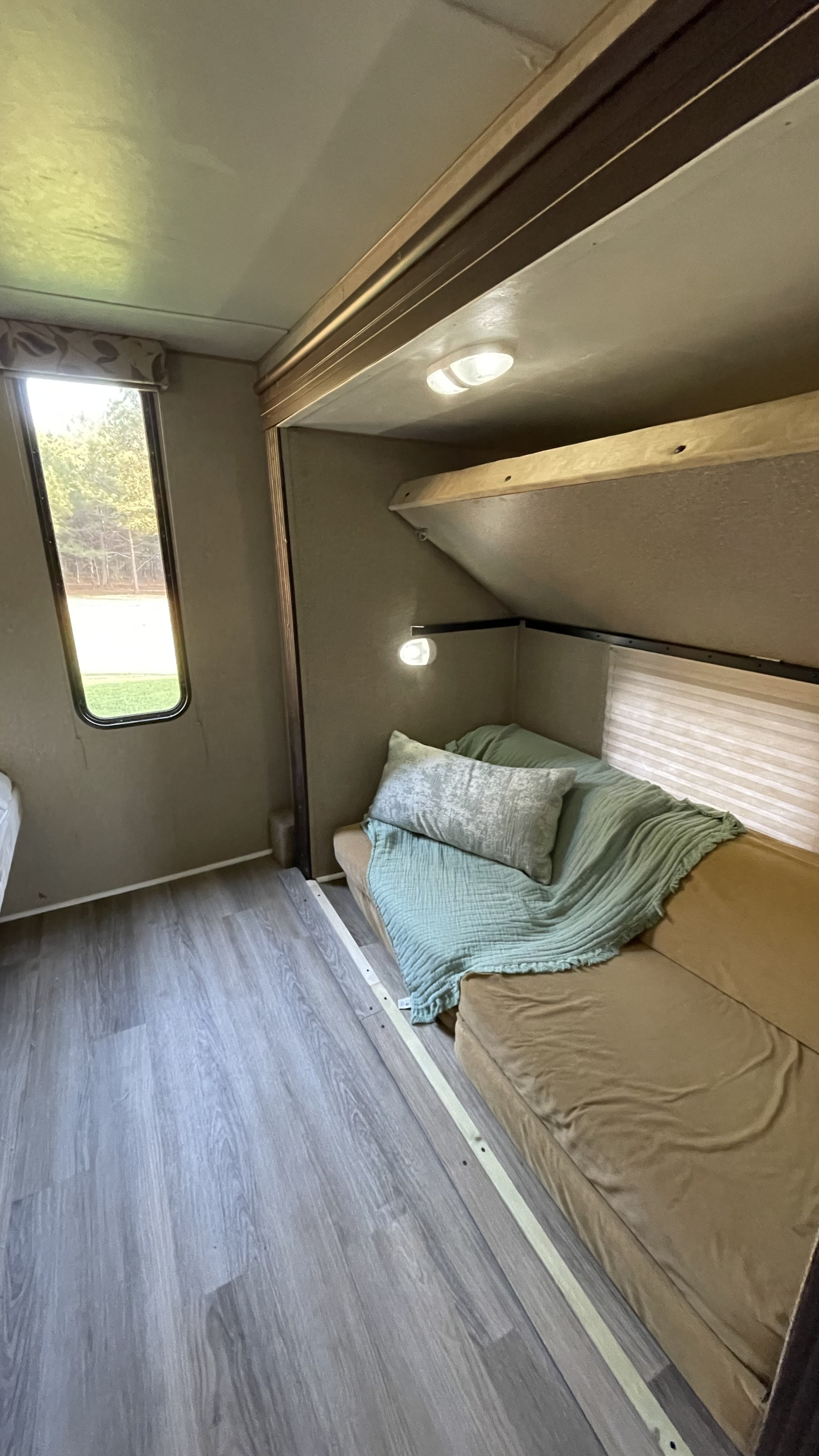 Cozy RV rental interior: bunk bed above a couch with green blanket, window view, and light wood-look flooring.. Forest River Cherokee 2016