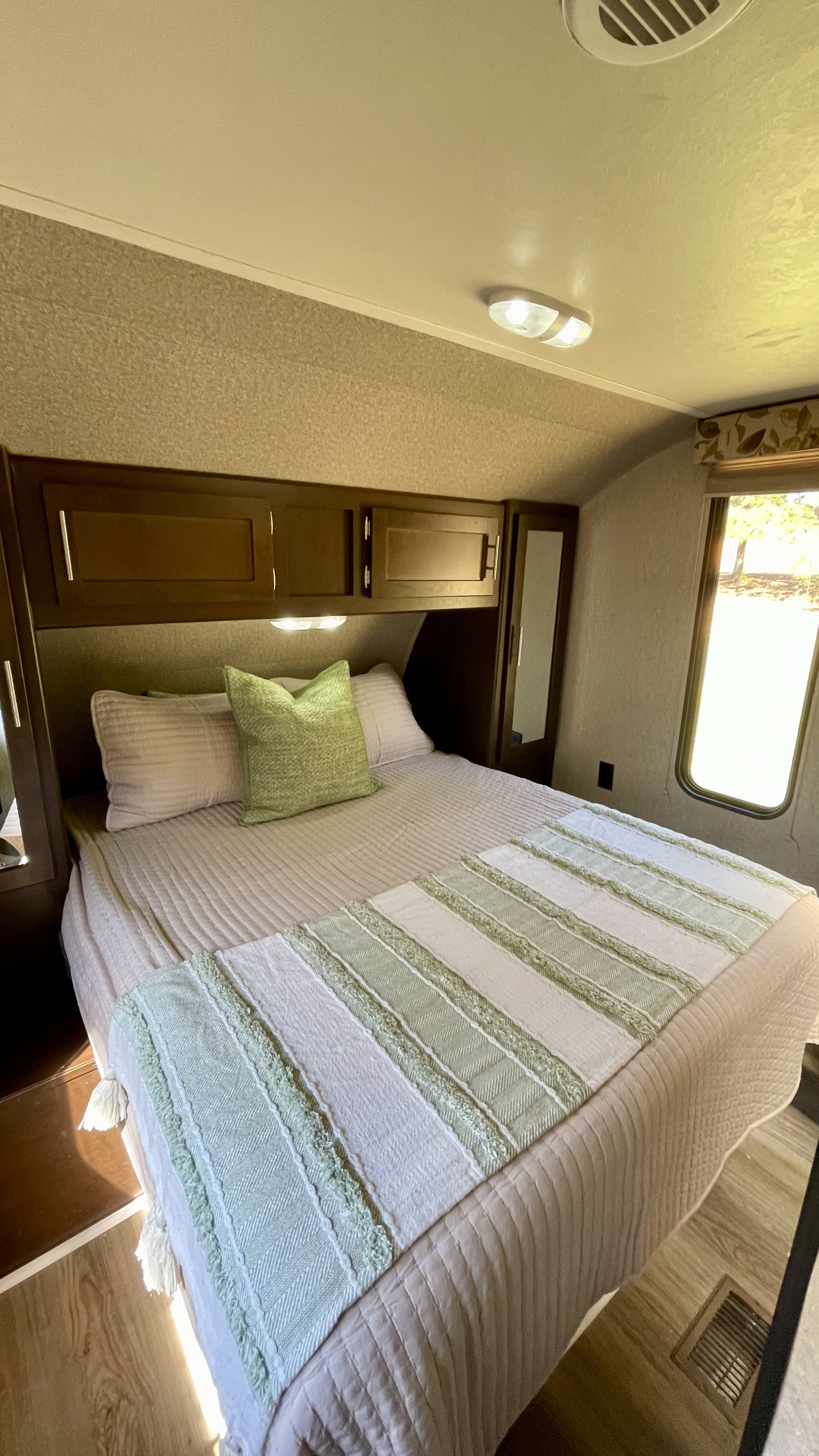 Step into a cozy RV rental bedroom with a comfy bed, light bedding, green accents, overhead cabinets, and a sunlit window.. Forest River Cherokee 2016