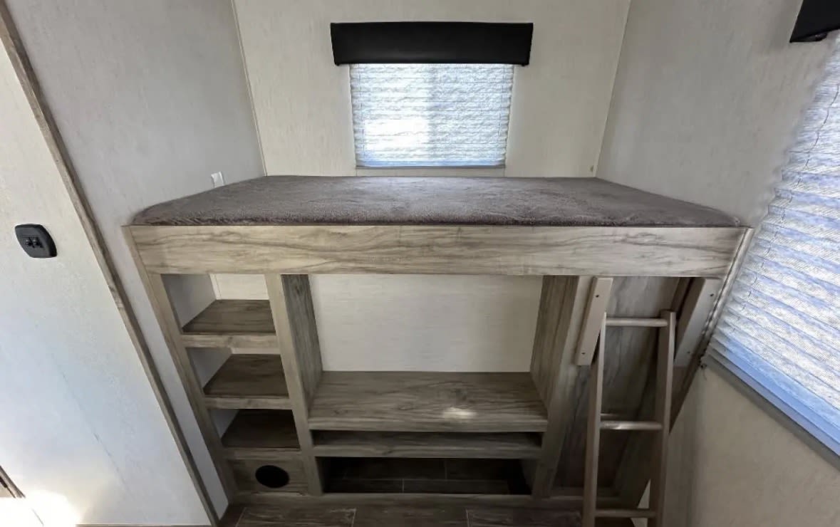 RV rental bunk bed with built-in shelves, ladder, and window; a compact and functional sleeping area.. Forest River Forest rivee 2022