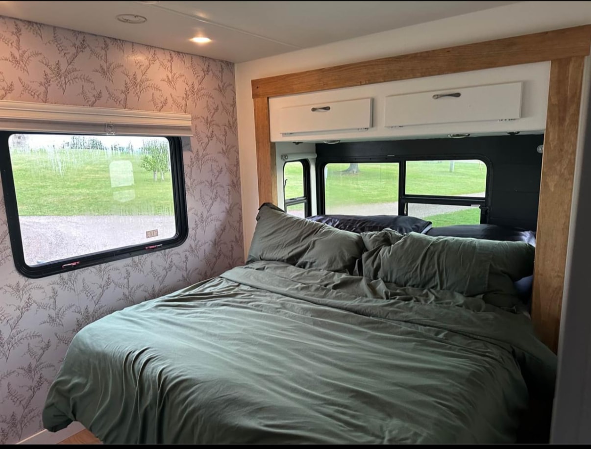 Modern RV rental bedroom. Features green bedding, fern wallpaper, white cabinets, and bright scenic windows, ideal for travel.. Georgetown ForestRiver 2009