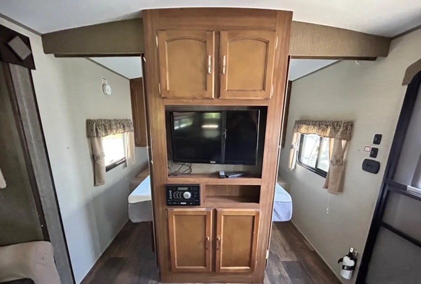 This RV rental's interior shows a compact bedroom area with a central wooden entertainment unit, TV, stereo, and beds.. Keystone RV Springdale 2016
