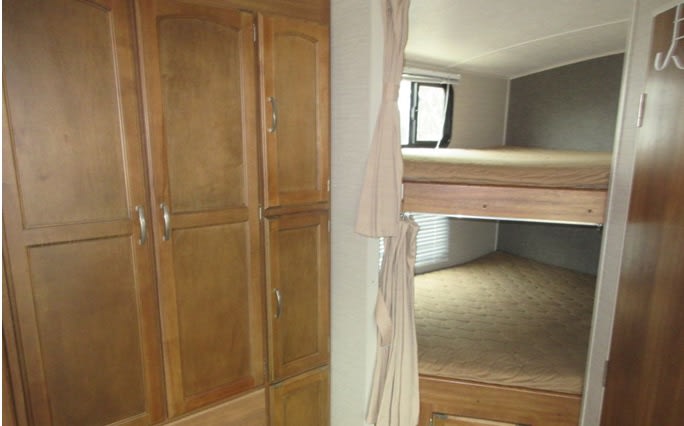 RV rental interior featuring wooden cabinets and a cozy bunk bed sleeping area with mattresses, perfect for camping.. Keystone RV Springdale 2016