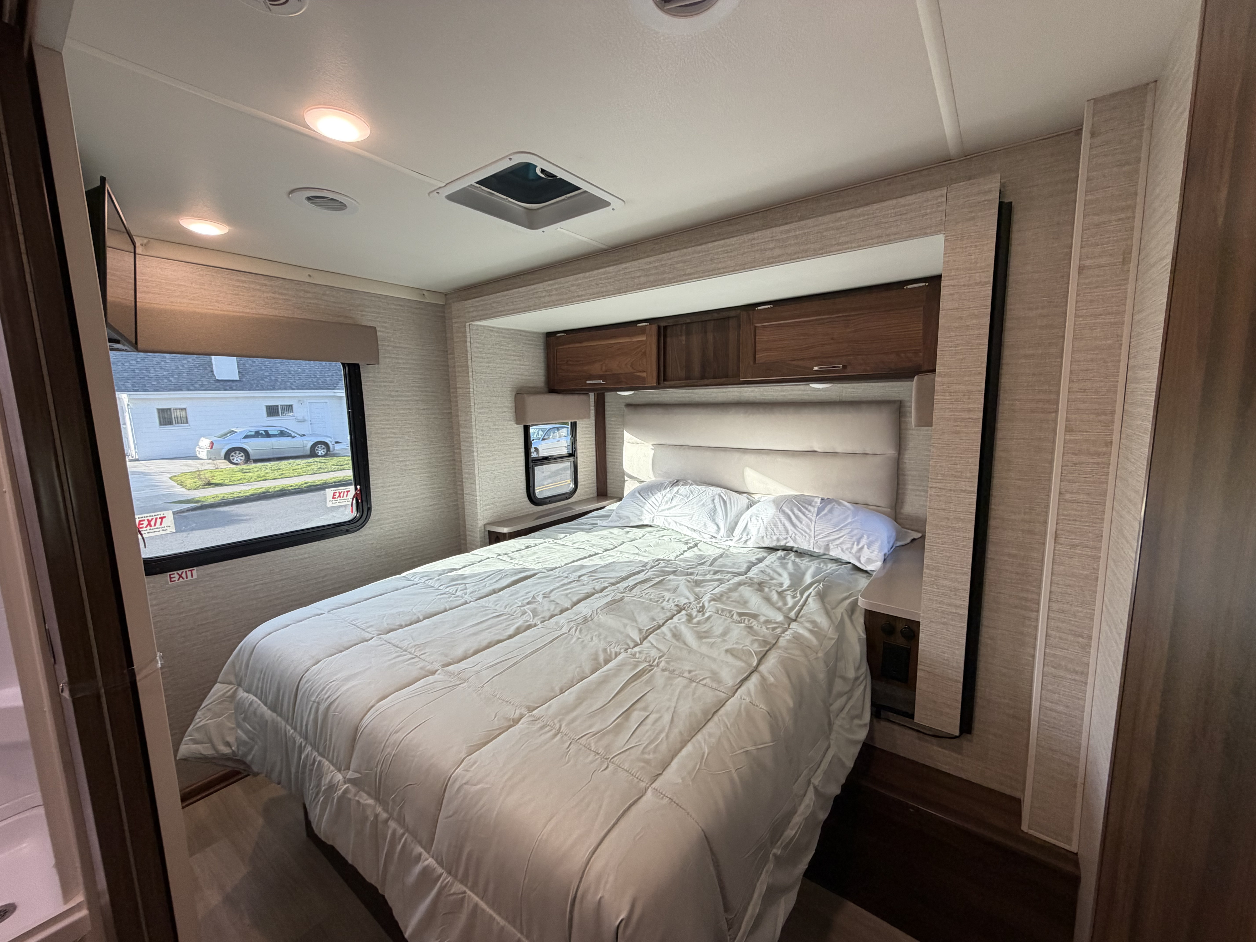 RV rental bedroom: a comfortable bed with white bedding, wood cabinets, and two windows offering natural light.. Winnebago Minnie Winnie 2025