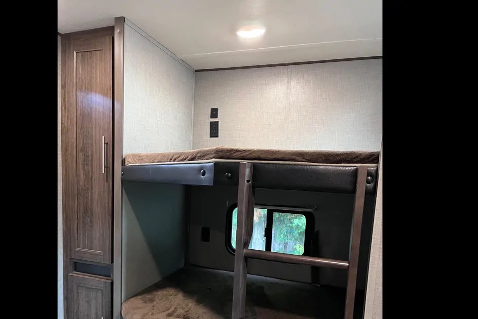 Inside an RV rental: cozy bunk beds with a ladder, window, and storage cabinet, featuring power outlets.. Crossroads RV zinger 2019