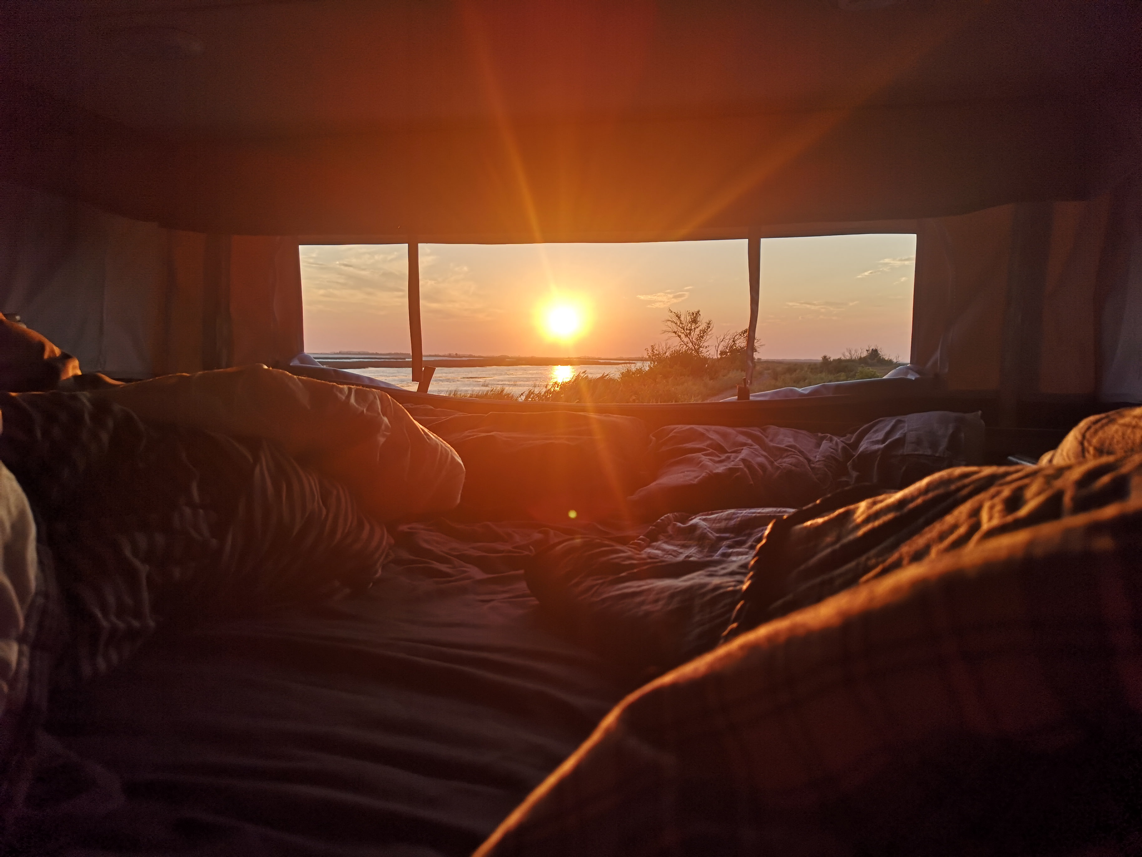 Breathtaking **sunrise** over water from a cozy **rv rental** bed. Experience **camping travel** with stunning **nature views**.. Palomino Real-Lite 2018