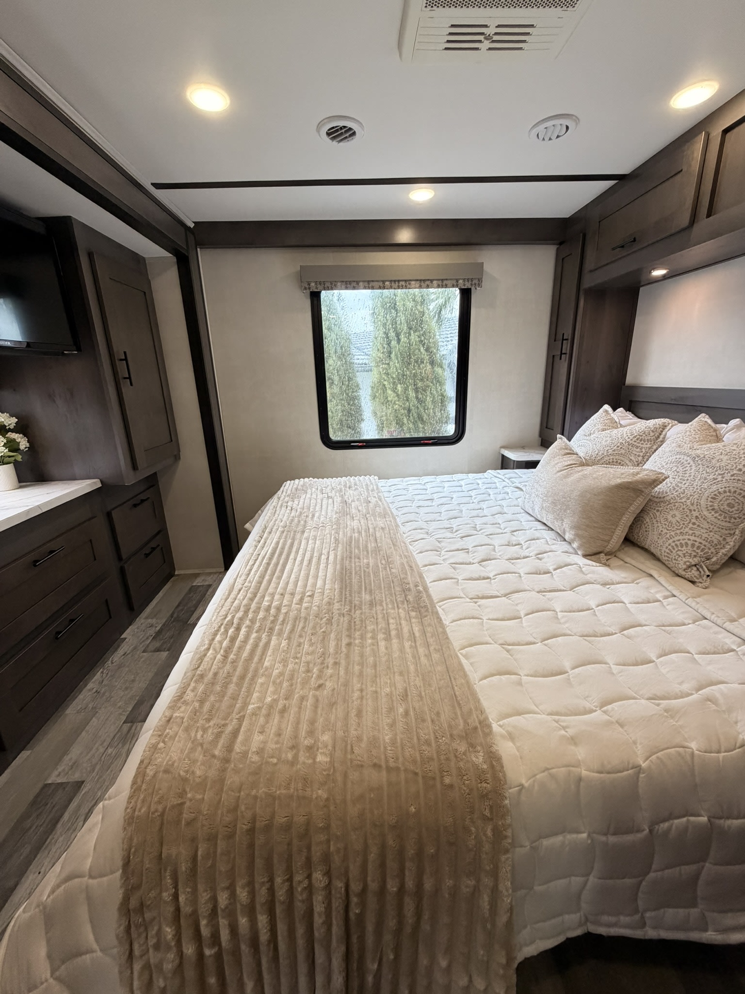Inviting RV rental bedroom with a comfortable bed, dark wood storage, modern lighting, and a scenic window view.. Forest River FR3 2023