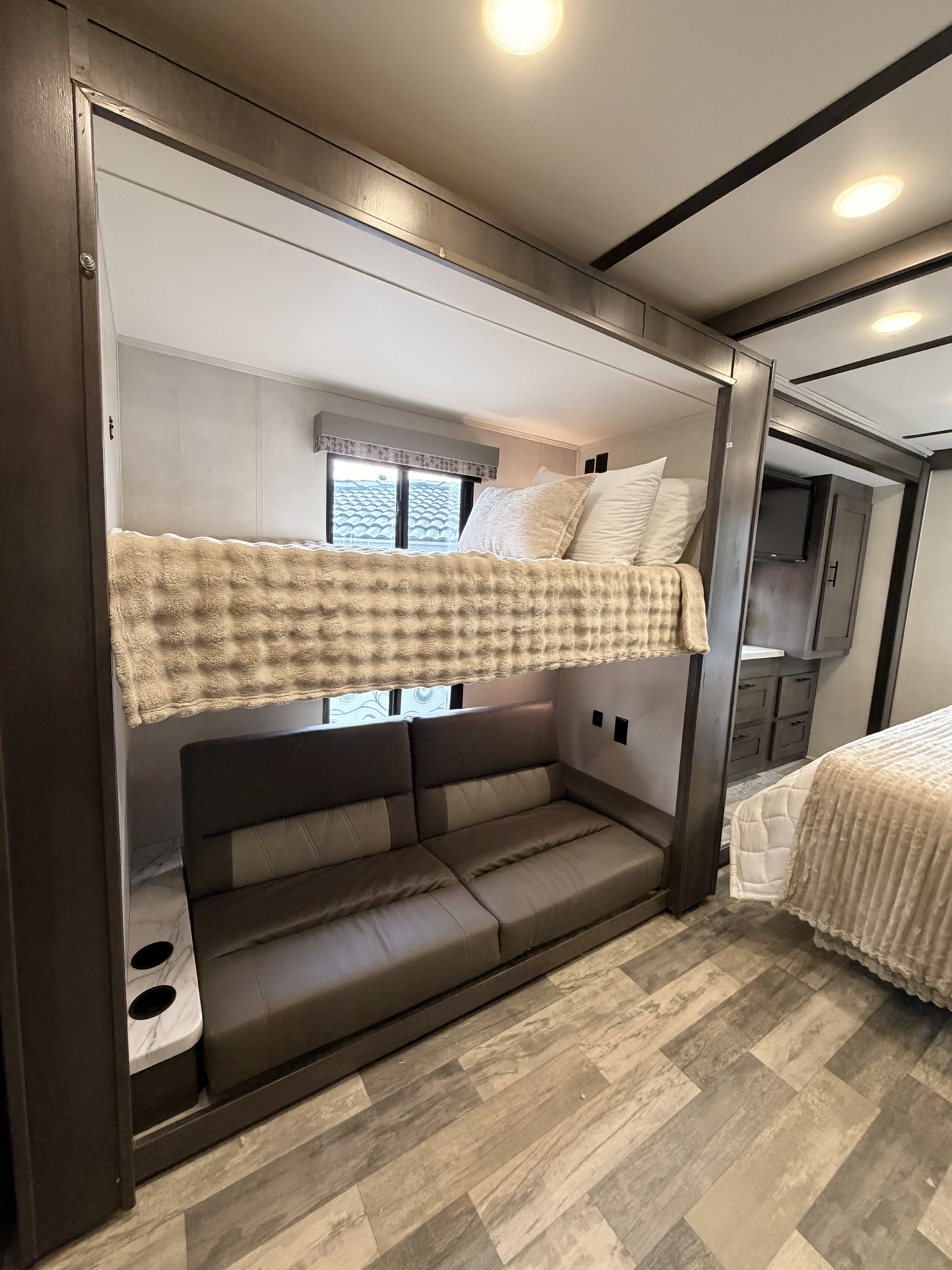 This RV rental features a cozy interior with bunk beds above a sofa, a separate bed, and modern wood-look flooring.. Forest River FR3 2023