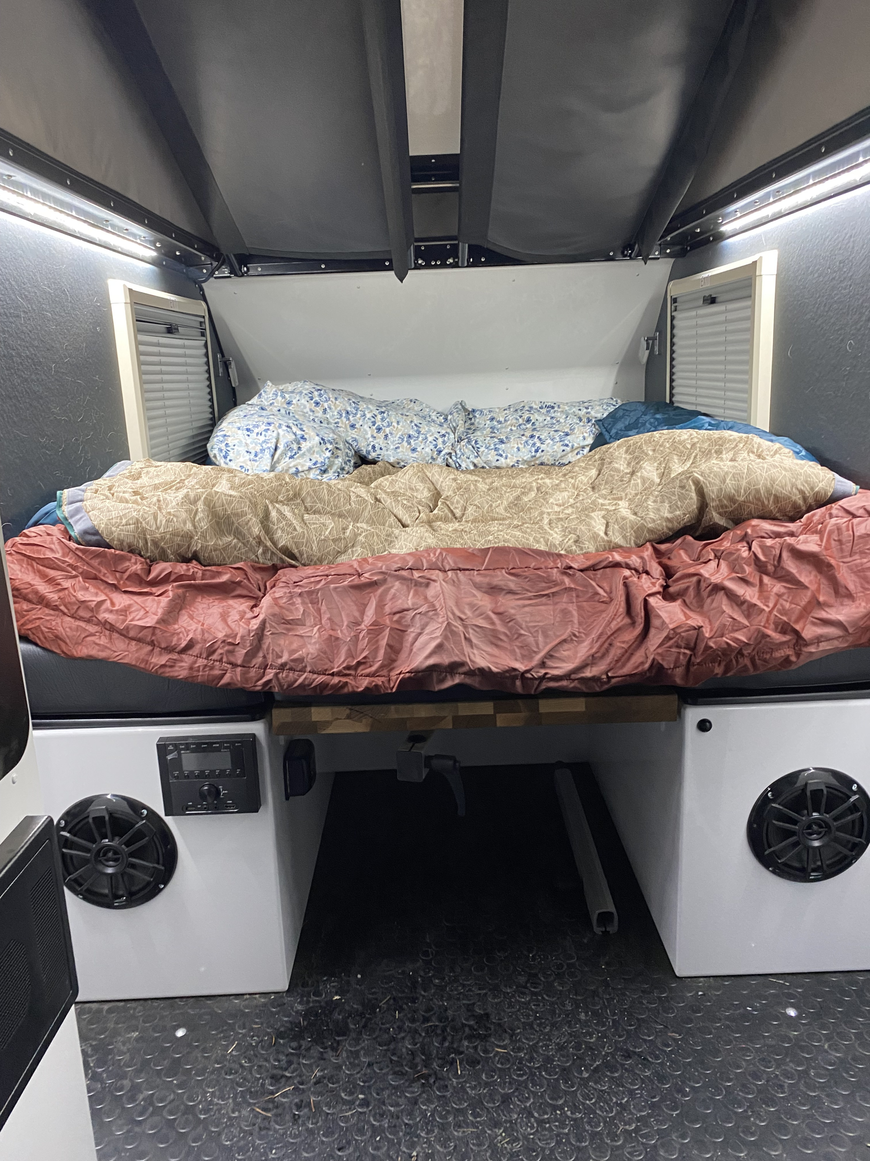 Cozy rv rental sleeping area features a bed with layered bedding, integrated lighting, side vents, and a compact audio system.. Mission Overland Mission Overland Trailer 2023