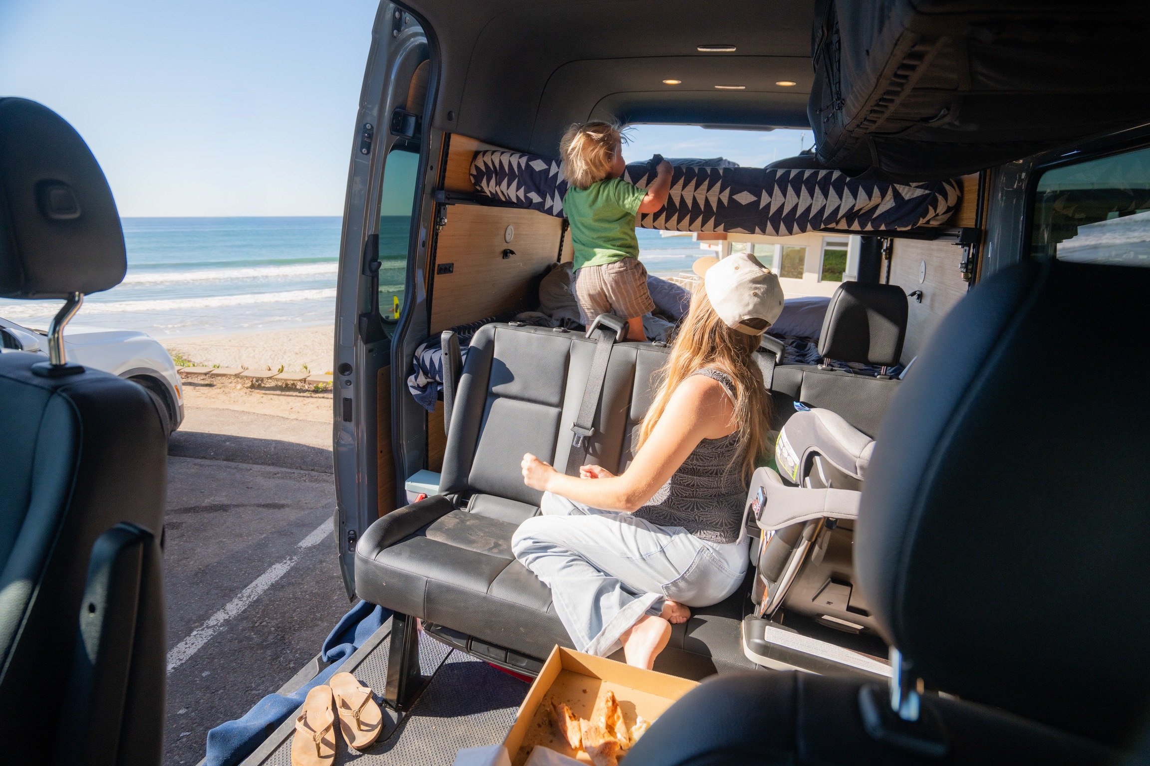 RV rental adventure: A family relaxes inside a camper van, with a child on the bunk and an adult enjoying the ocean view.. Mercedes sprinter 2025