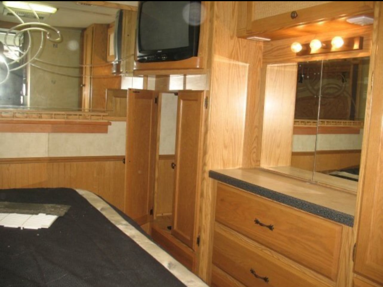 RV rental bedroom features wooden cabinetry, a mounted TV, lighted mirror, and practical drawers for a cozy, functional space.. Safari Simba 2004