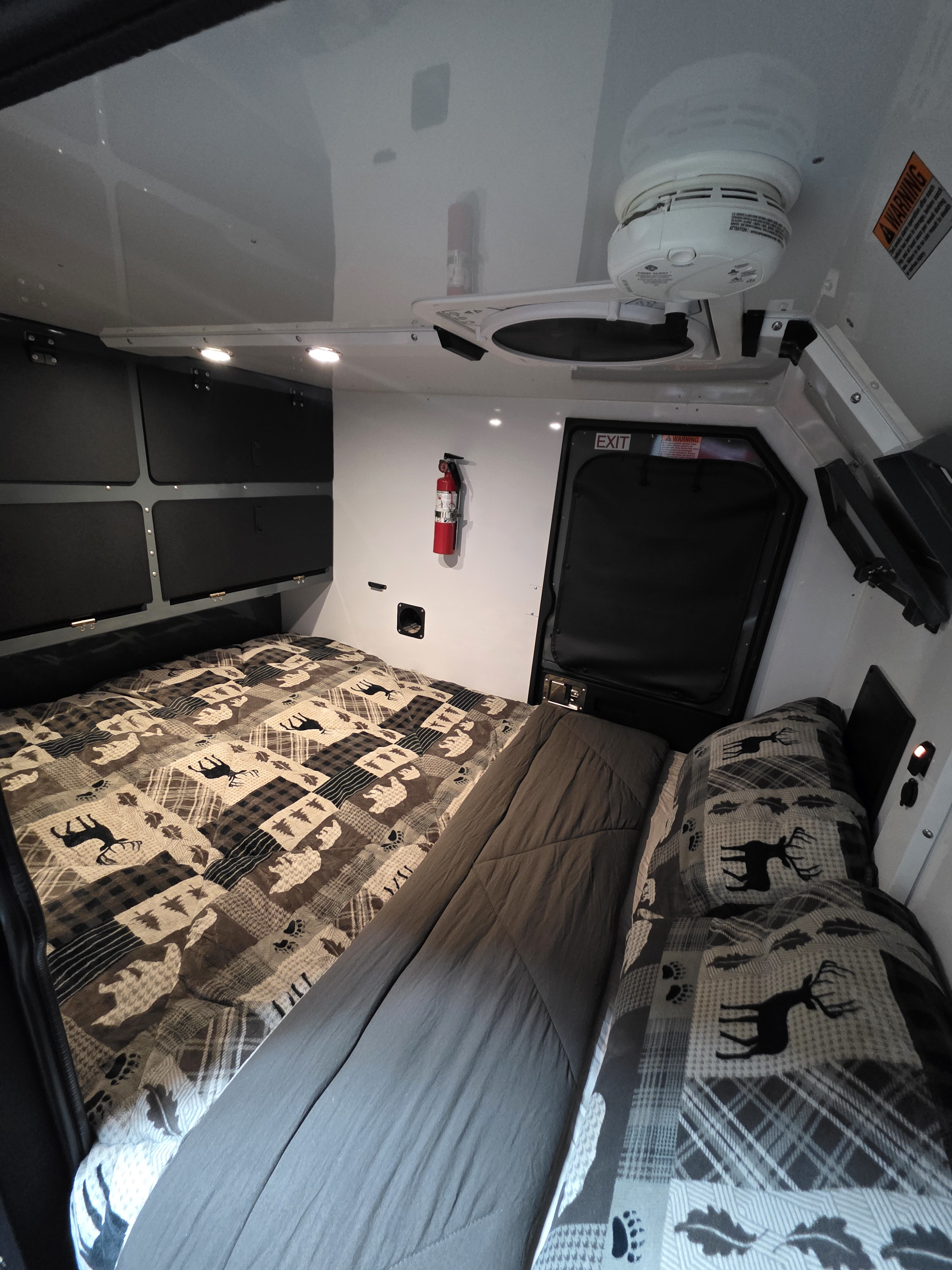 RV rental interior features patterned bedding, overhead storage, a fire extinguisher, and a smoke alarm for safety.. Off Grid Trailers Sprocket X 2023