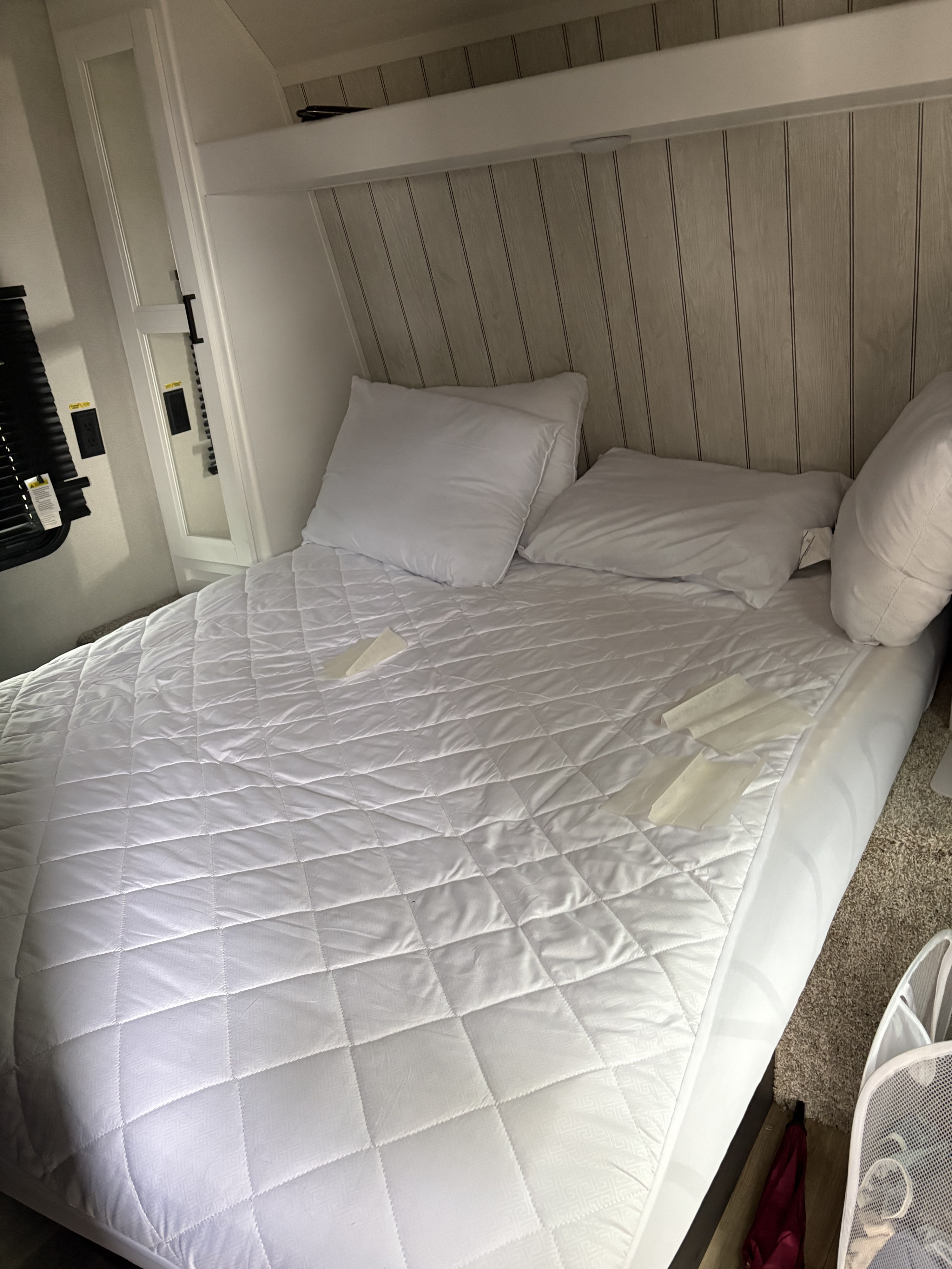 Cozy RV rental bedroom features a white quilted mattress pad, pillows, and wood paneling in a compact sleeping area.. Keystone RV Hideout 2022