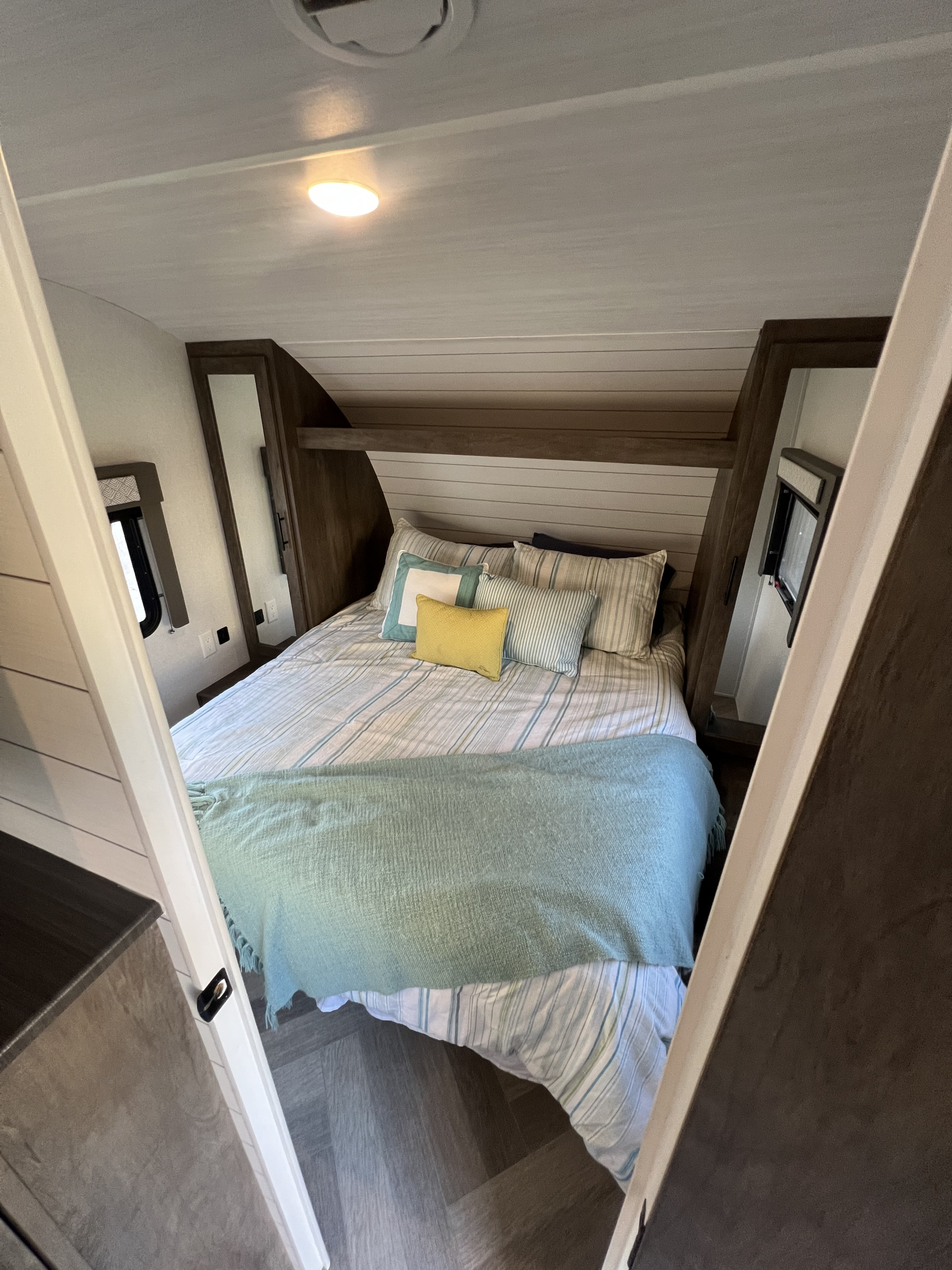 Modern RV rental bedroom features a cozy bed with striped linens, blue throw, built-in shelf, and windows. Ideal for travel.. Forest River Wildwood X-Lite 2020