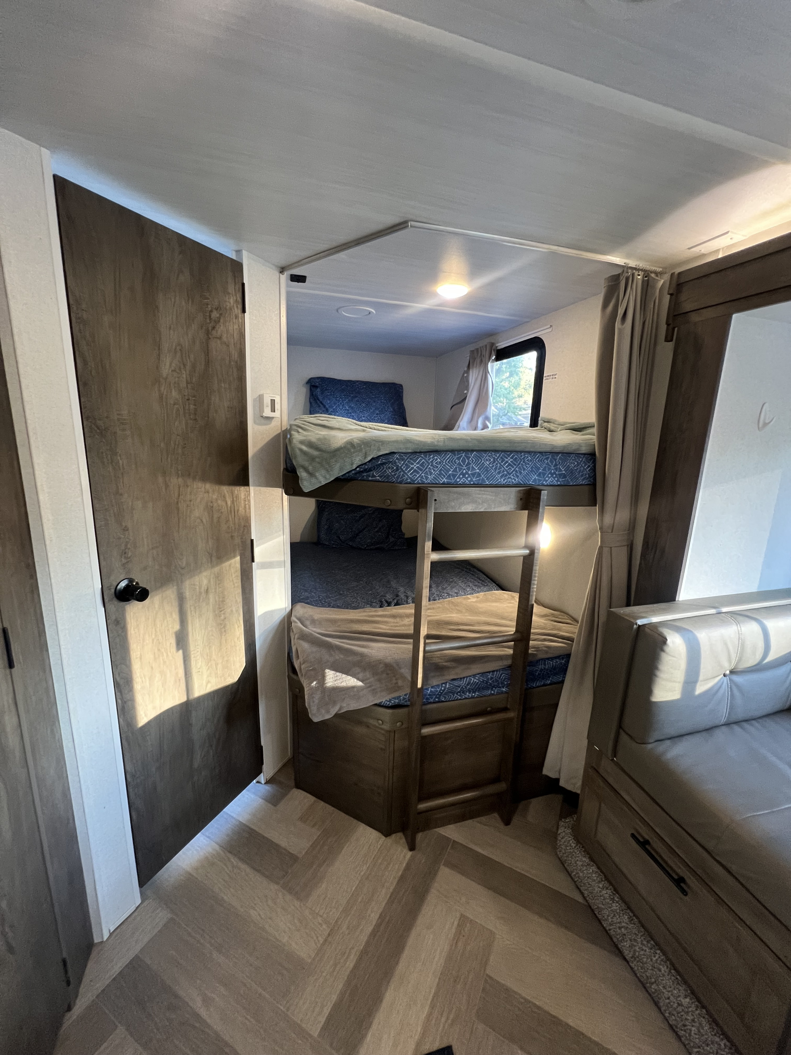 RV rental interior featuring cozy bunk beds with a ladder, window, and adjacent seating area.. Forest River Wildwood X-Lite 2020