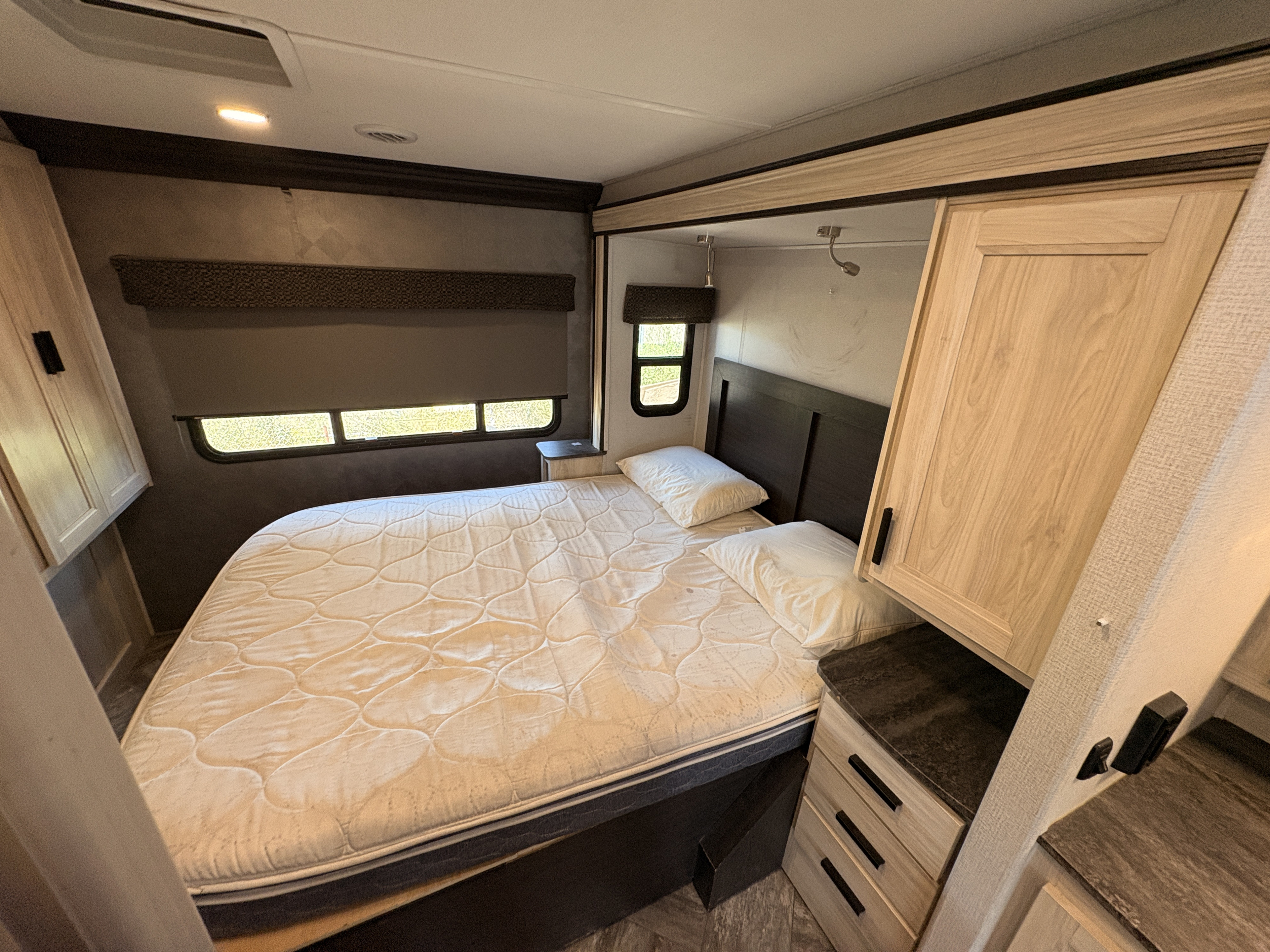 Inside a cozy RV rental bedroom: a bed with white bedding, windows, and light wood cabinets, designed for comfortable travel.. Forest River Sunseeker Classic 2022