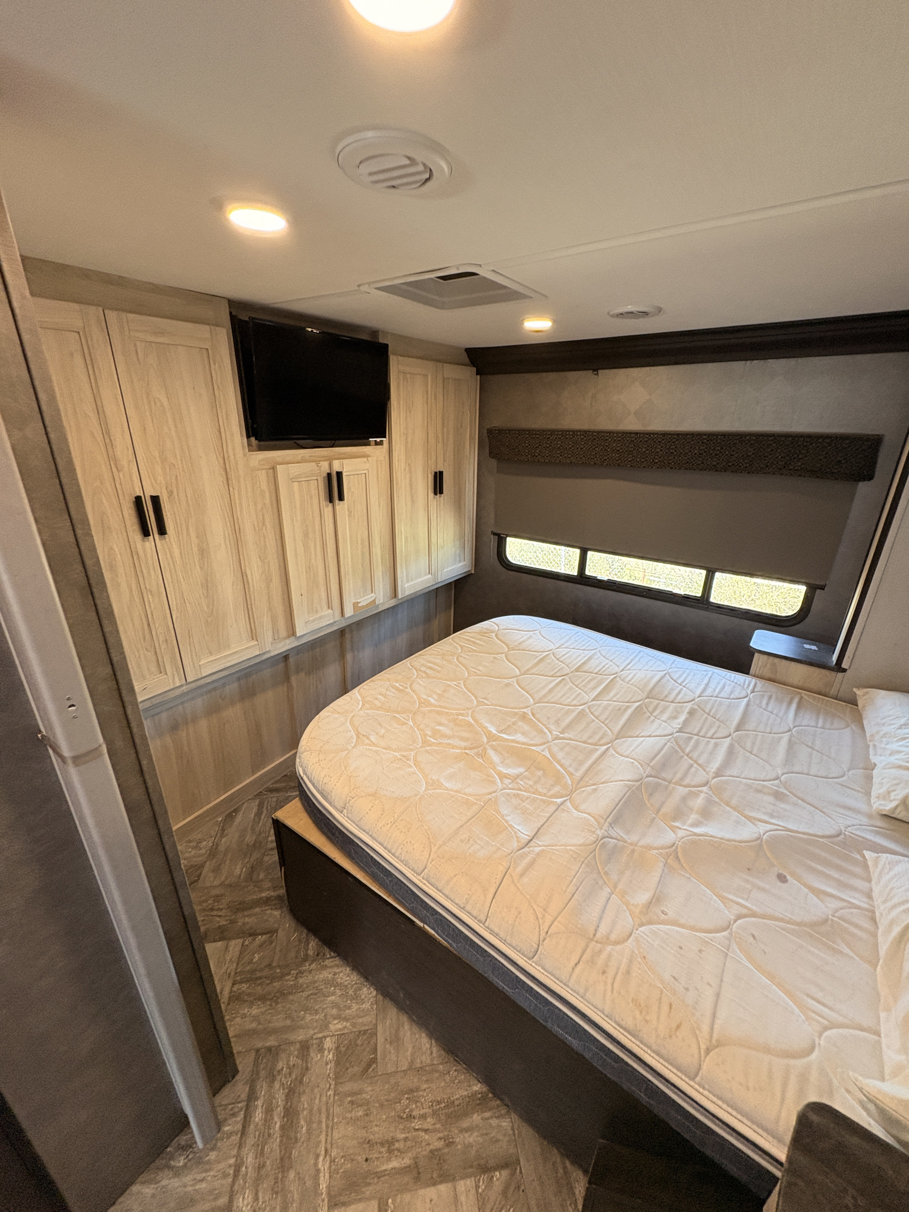 RV rental bedroom with light wood cabinets, TV, and a queen mattress. Includes window with shades and ceiling vents.. Forest River Sunseeker Classic 2022