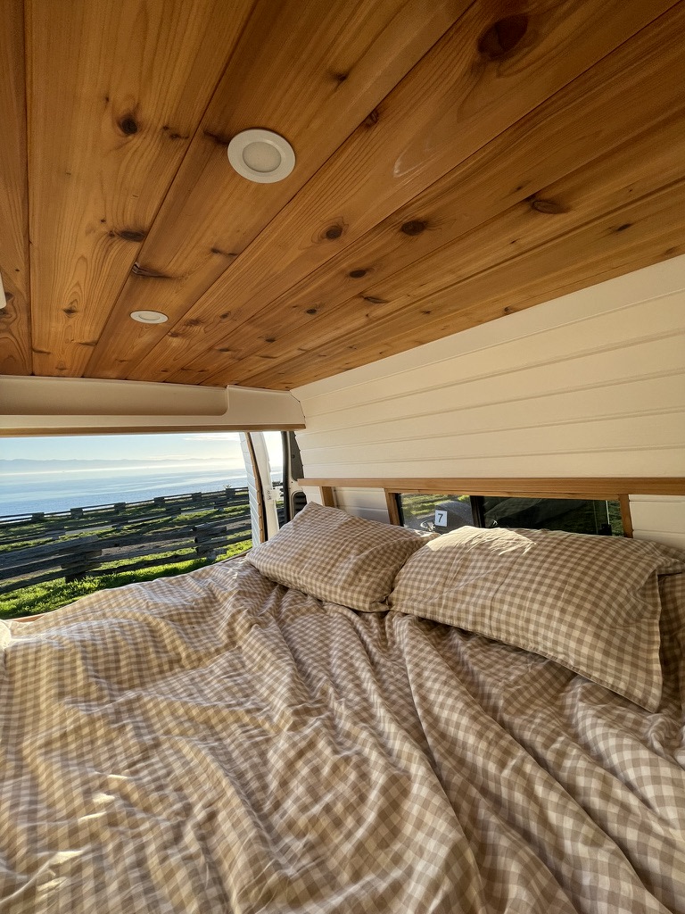 Cozy RV rental bed with a stunning ocean view, perfect for van life adventures.. Ram Promaster 3500 2018