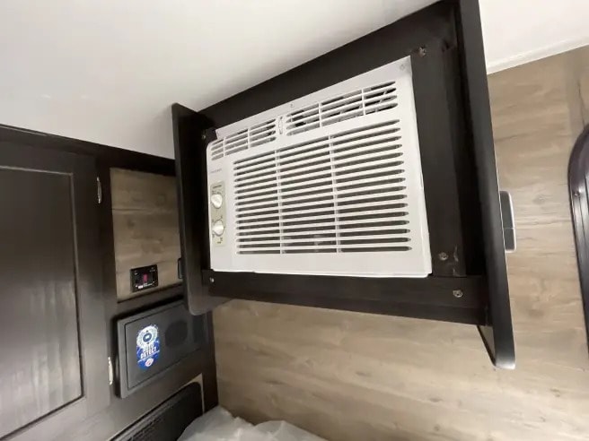 RV rental interior: A window AC unit installed in an overhead cabinet, with a digital control panel and safe below.. Braxton Creek Bushwhacker 2024