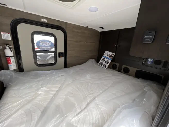 New RV rental bedroom featuring a plastic-wrapped mattress, entry door, fire extinguisher, and interior controls.. Braxton Creek Bushwhacker 2024