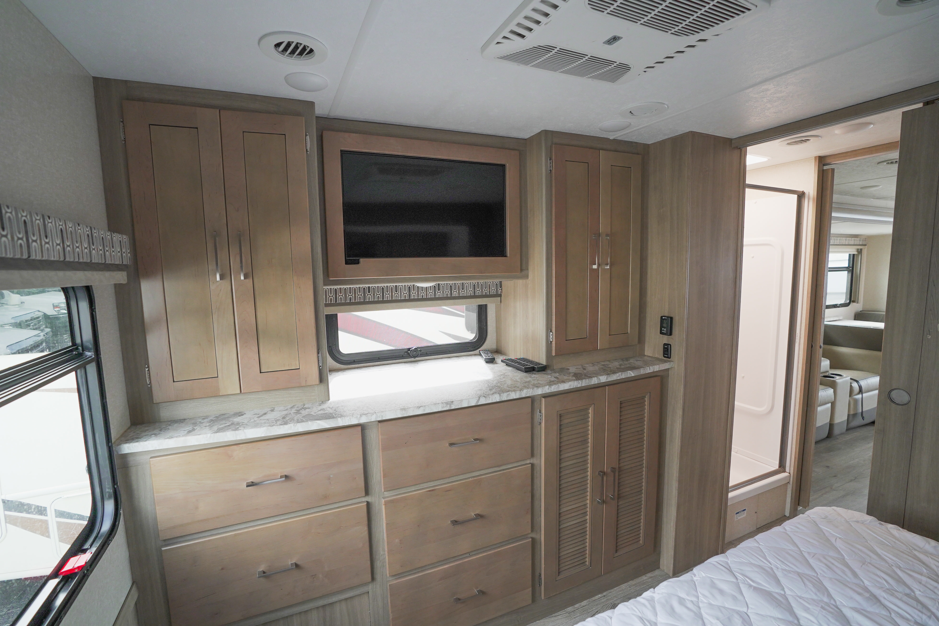Modern RV rental bedroom featuring ample wood storage, TV, and an adjacent shower, offering comfort on the road.. Coachmen Pursuit 2019