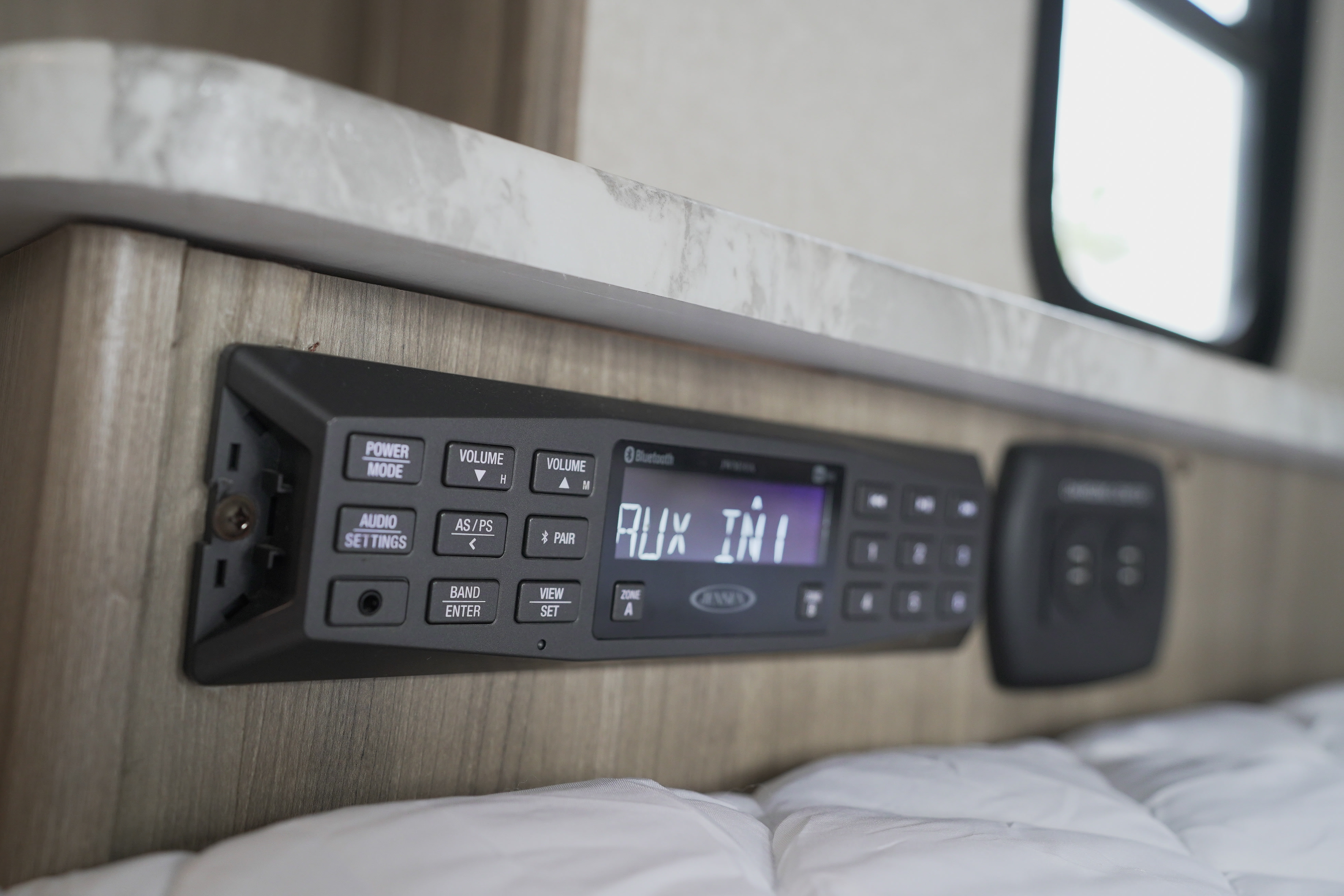 RV rental interior: a stereo control panel showing 'AUX IN1' on its screen. Buttons for power, volume, and Bluetooth are visible.. Coachmen Pursuit 2019