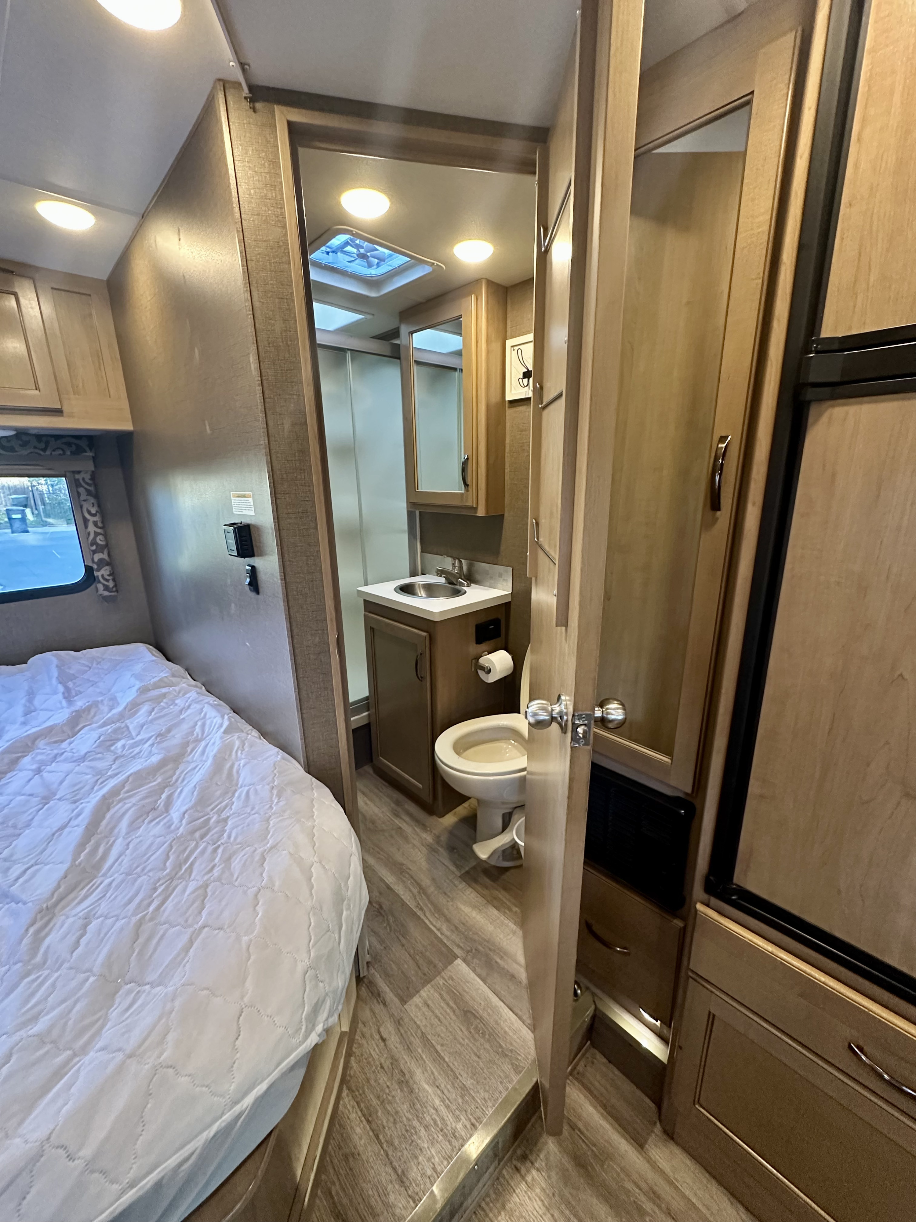 RV rental interior featuring a cozy bed, compact bathroom (toilet, sink, shower), and a refrigerator visible.. Thor Four Winds 2019