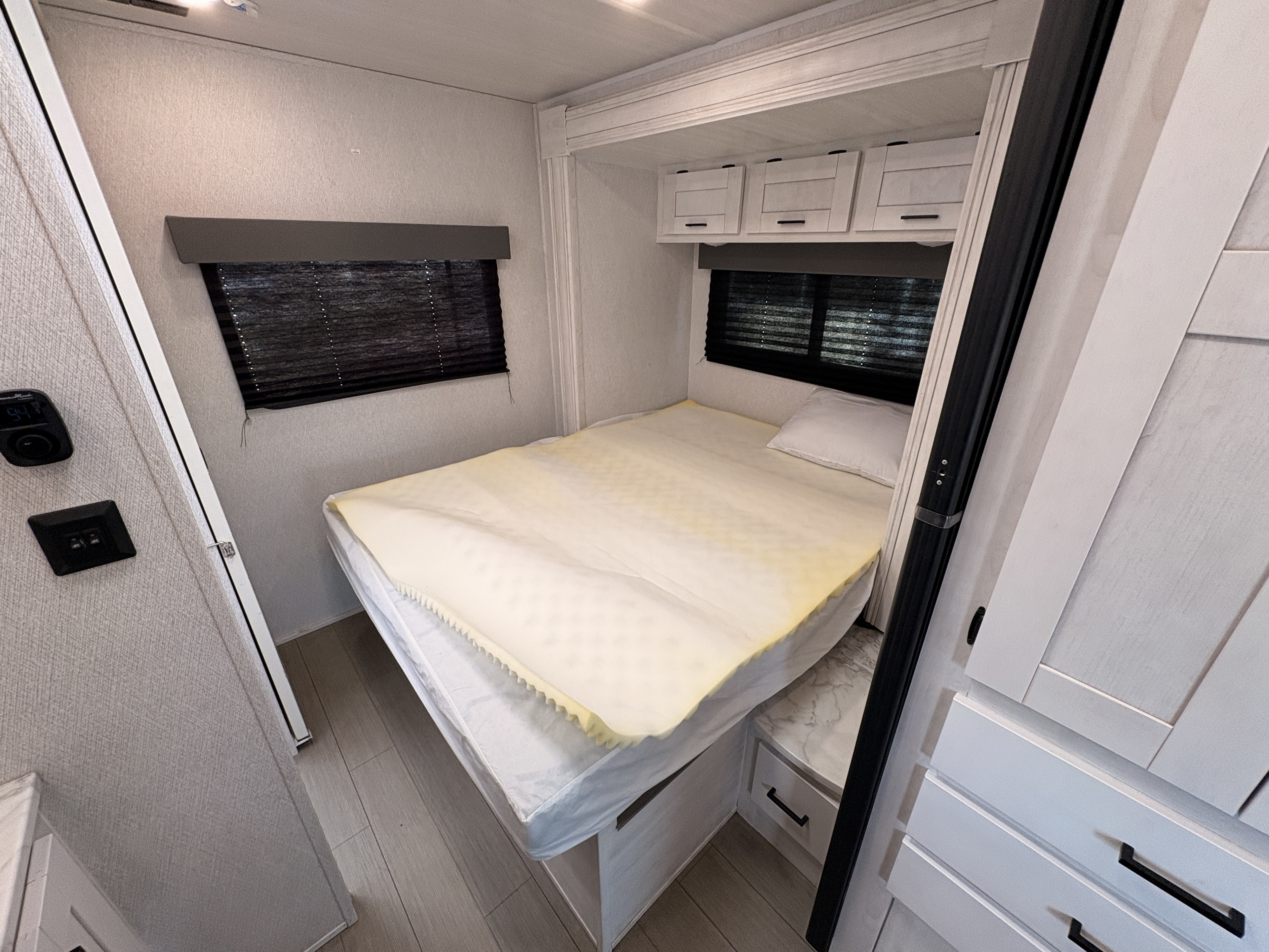 Inside an RV rental, a cozy bedroom with a bed, foam topper, window, and built-in storage offers compact comfort.. East to West Entrada 2024