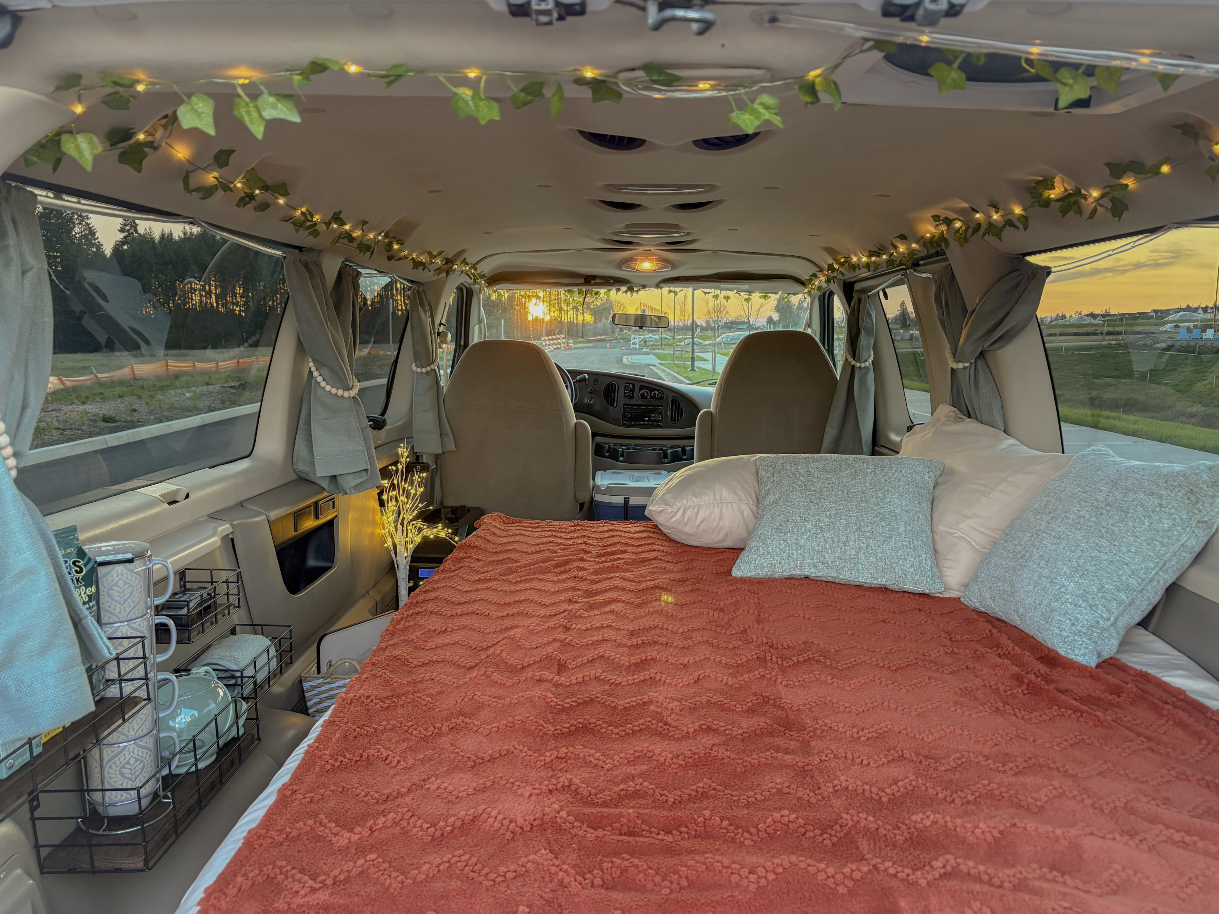 Inside a cozy RV rental: bed with textured blanket, fairy lights, and beautiful sunset views. Your home on wheels awaits!. Ford Econoline 2008