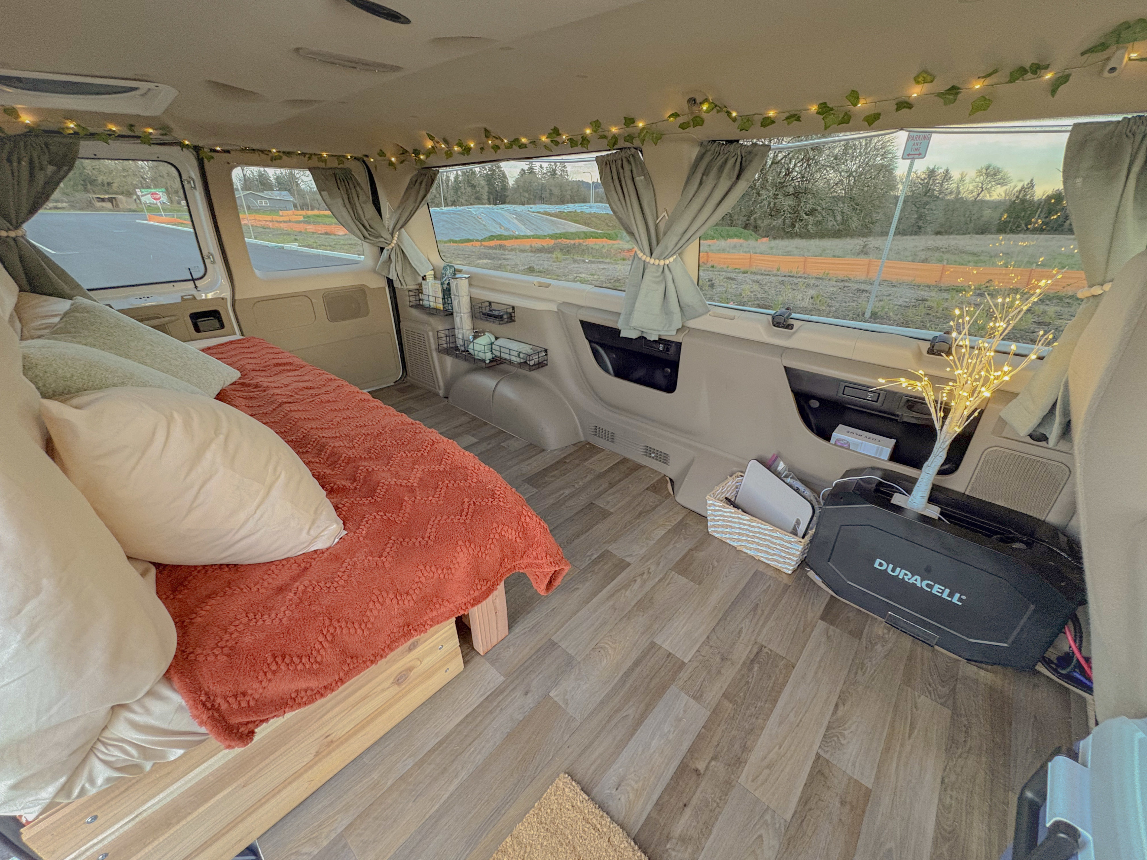 Cozy RV rental van interior featuring a bed with a warm blanket, string lights, curtains, and a Duracell power station.. Ford Econoline 2008