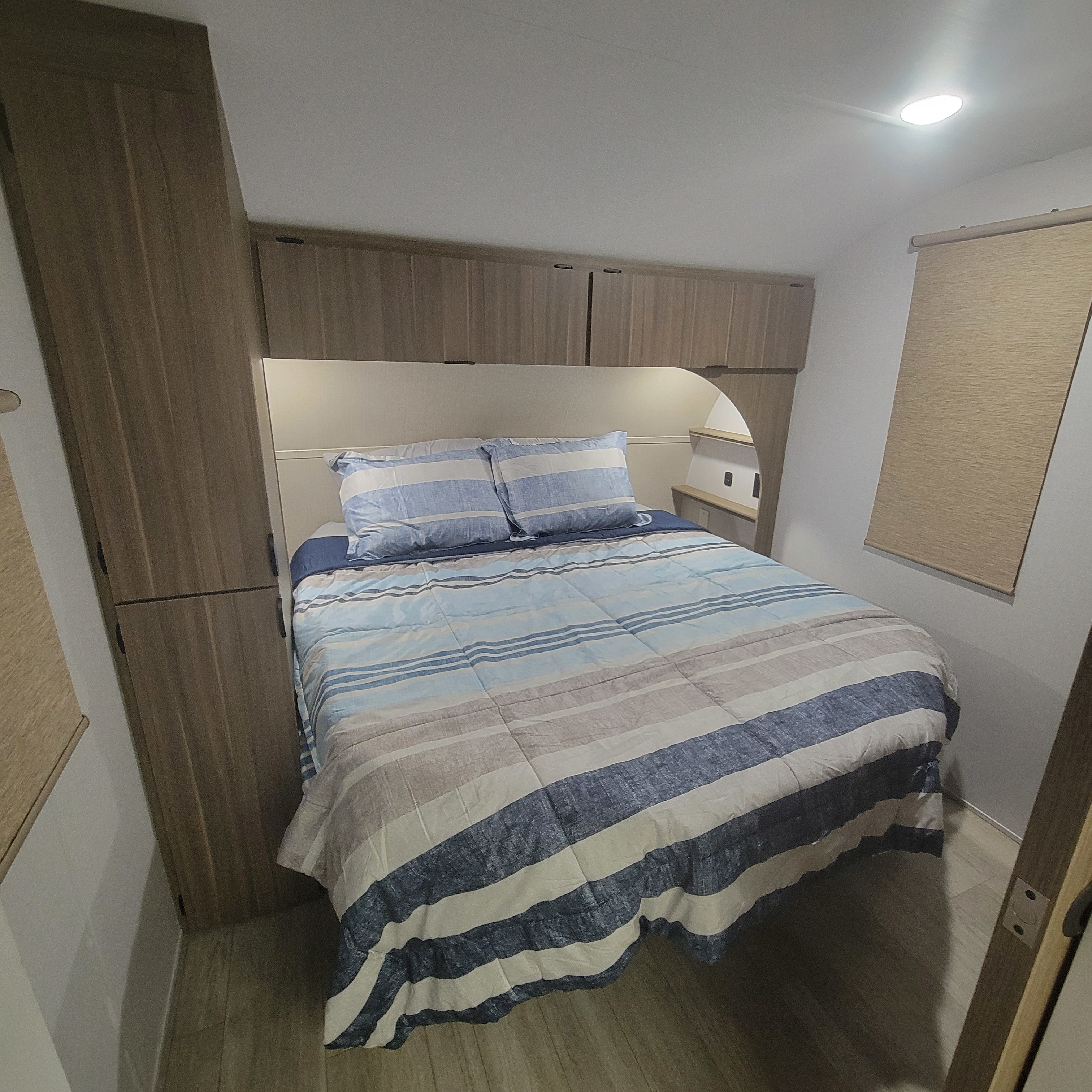 RV rental bedroom featuring a comfy bed with striped blue and beige bedding, built-in wooden cabinets, and a ceiling light.. Forest River Salem Cruise-Lite 2026
