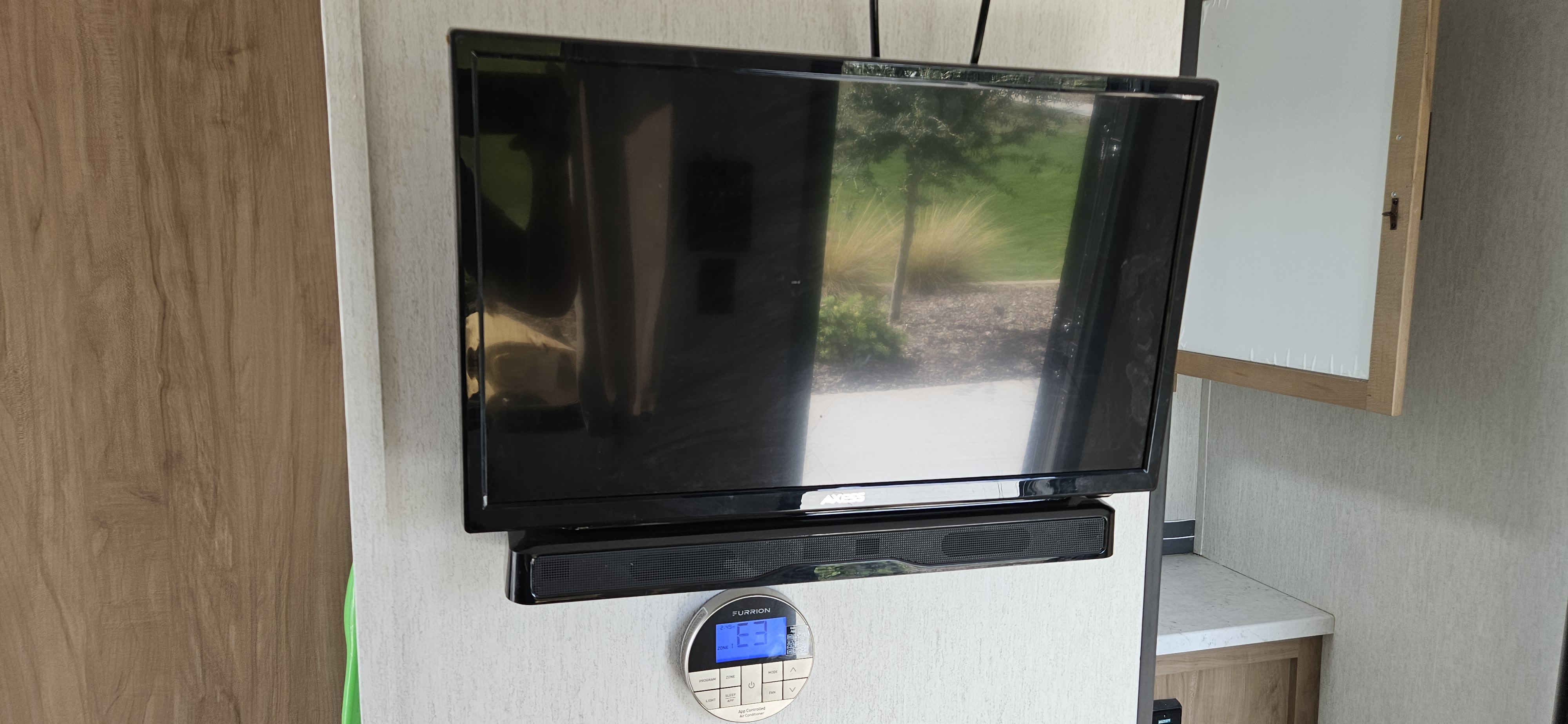 RV rental interior featuring a wall-mounted TV, soundbar, and climate control. Reflections show outdoors.. Forest River Cherokee Grey Wolf 2023