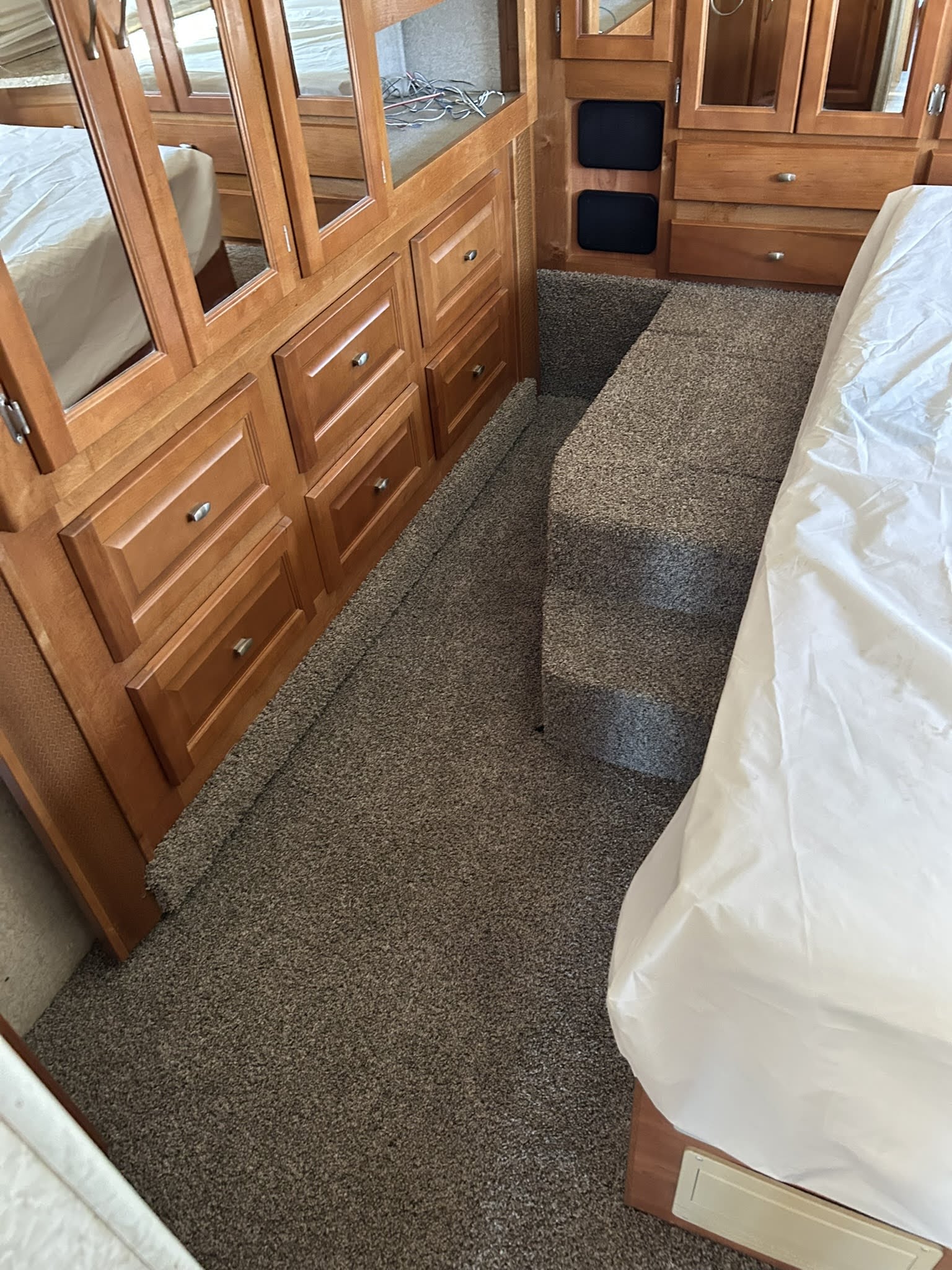 RV rental bedroom with raised bed, white sheets, carpeted steps, and warm wooden cabinetry with mirrored doors and storage.. Gulf Stream Tourmaster 2005